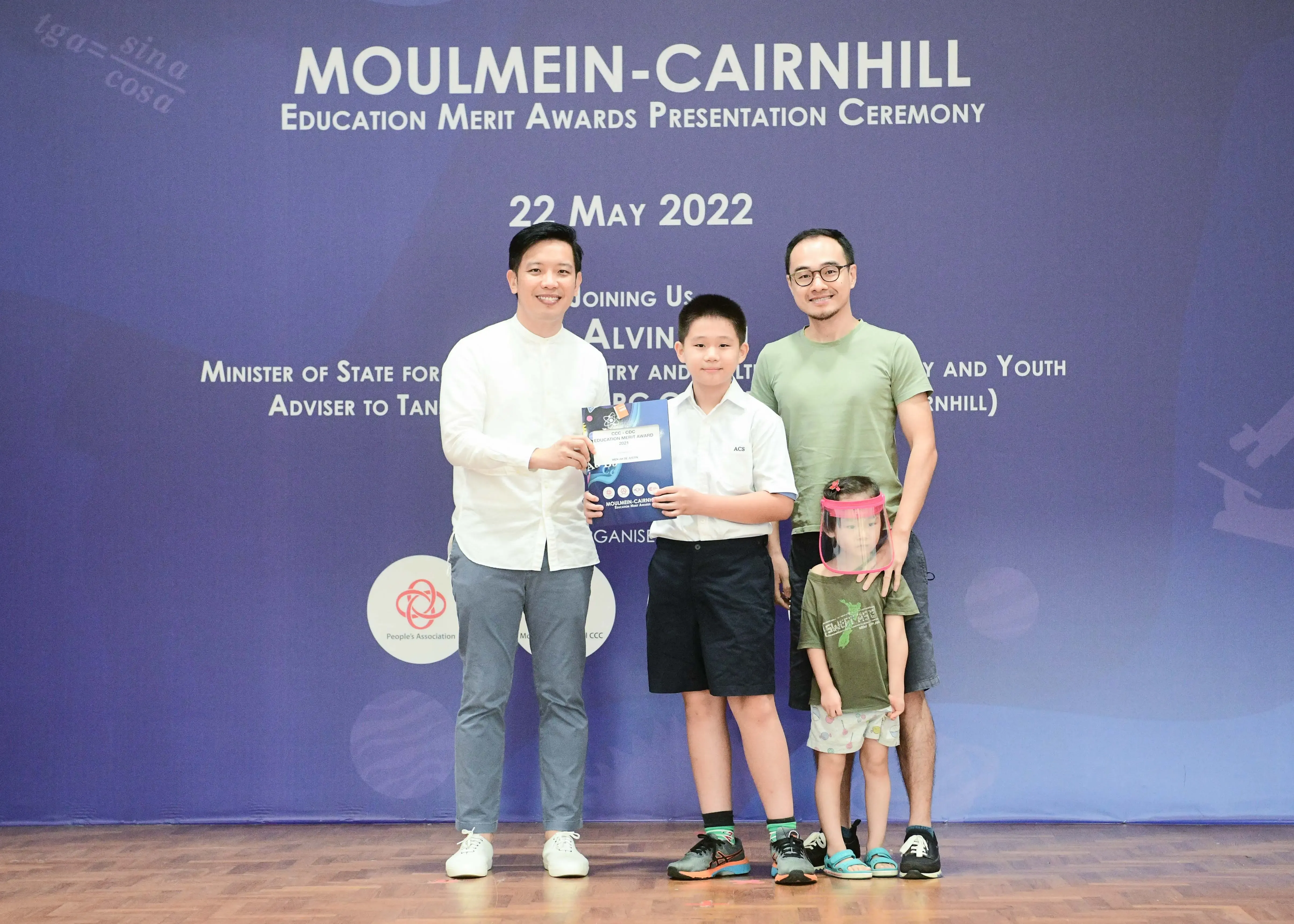 Four people pose at the Moulmein-Cairnhill Education Merit Awards Ceremony on 22 May 2022, with a boy holding a certificate.