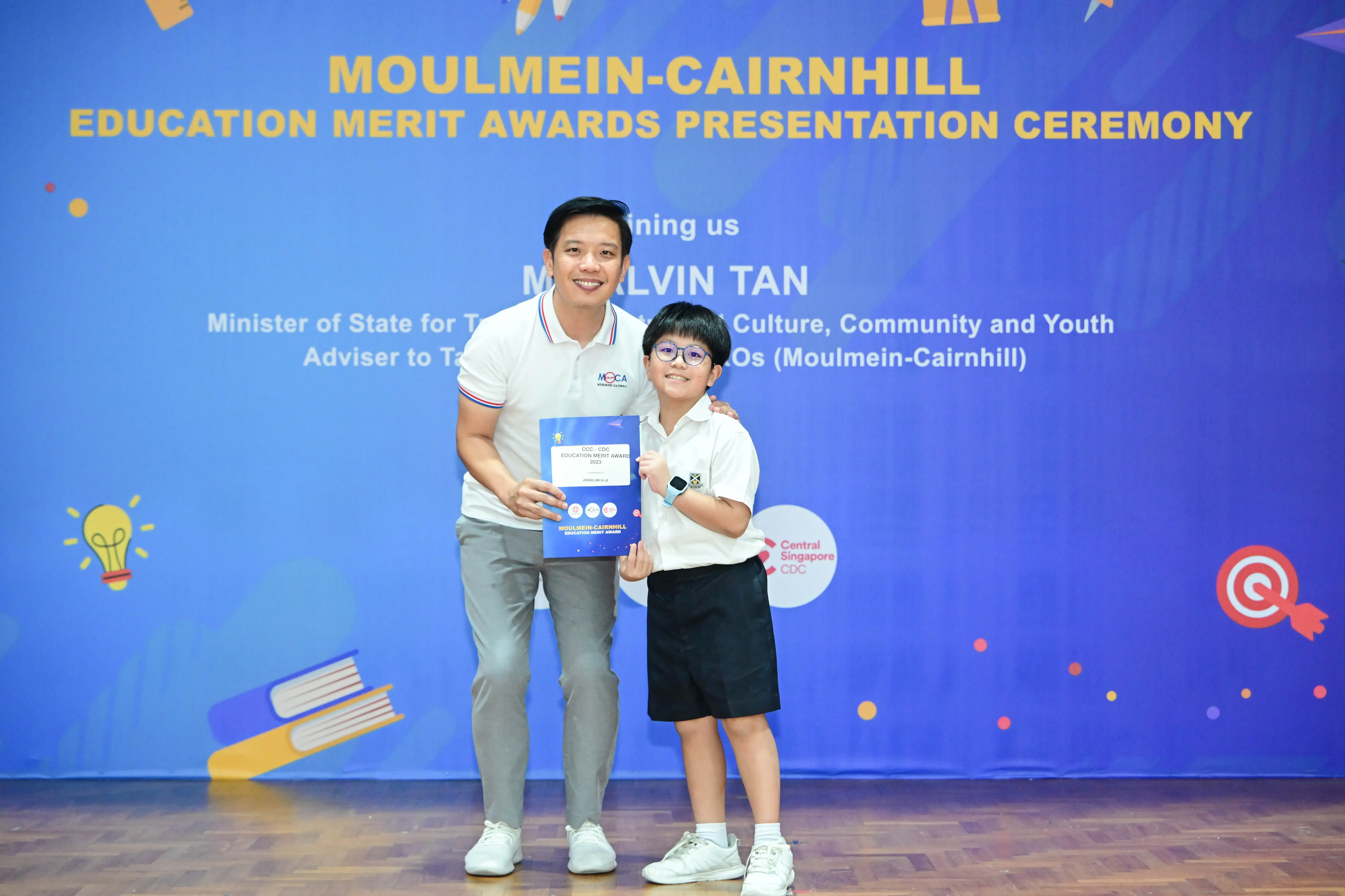 A man and a young student pose together holding a certificate at the Moulmein-Cairnhill Education Merit Awards ceremony.