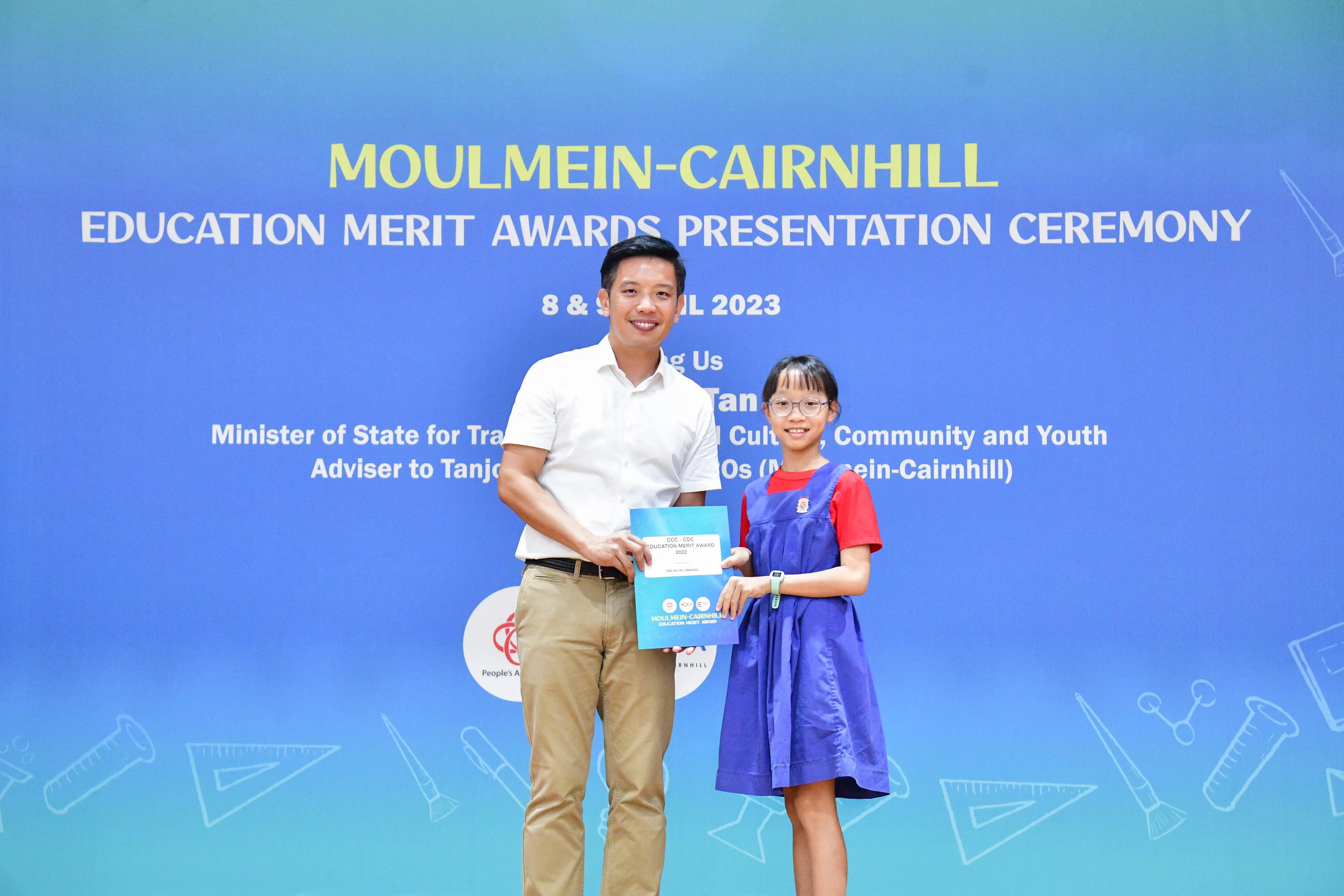 A man and a young girl hold an award certificate at the Moulmein-Cairnhill Education Merit Awards Ceremony 2023.