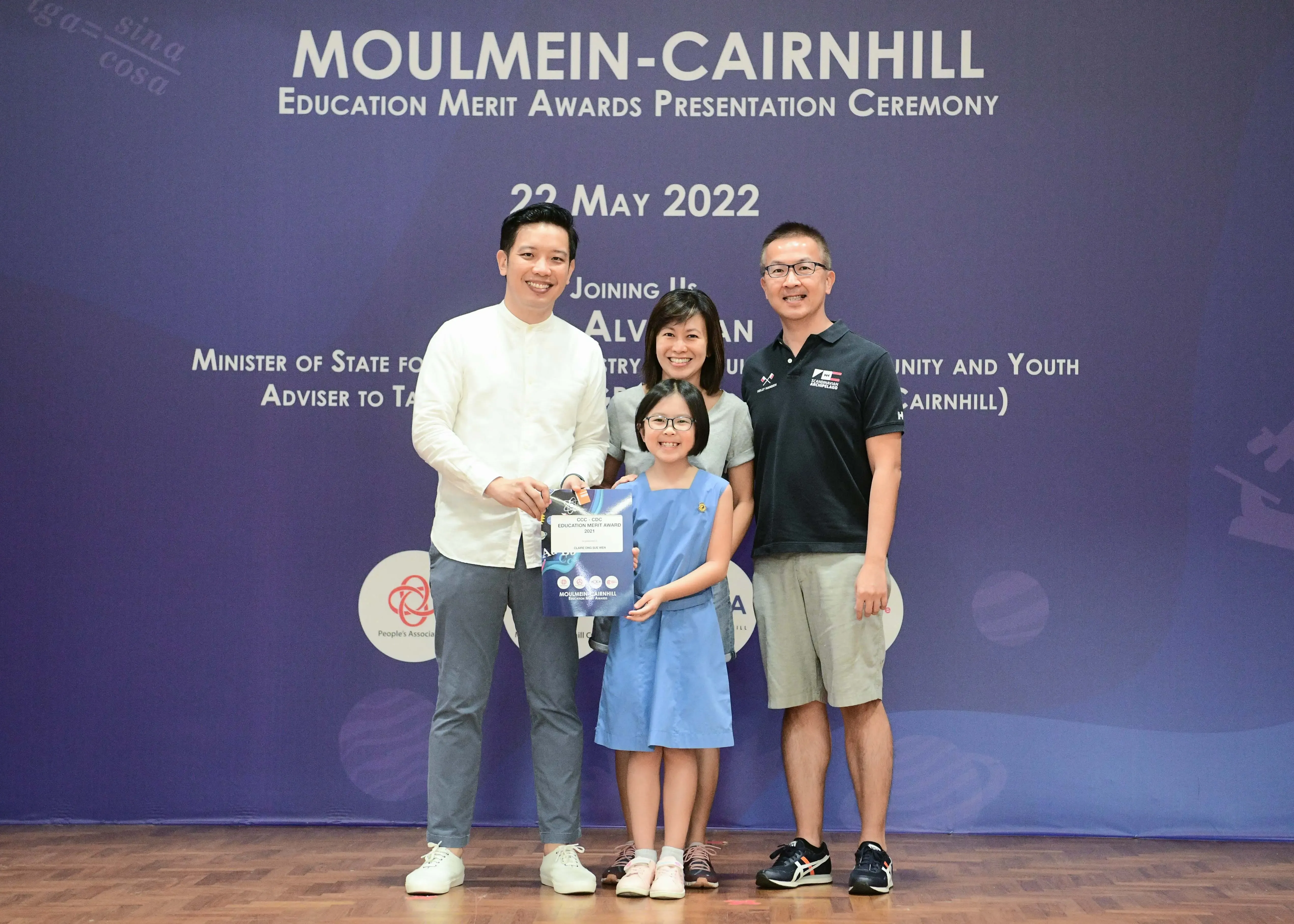Four people pose at the Moulmein-Cairnhill Education Merit Awards Ceremony on 22 May 2022, with a girl holding an award.