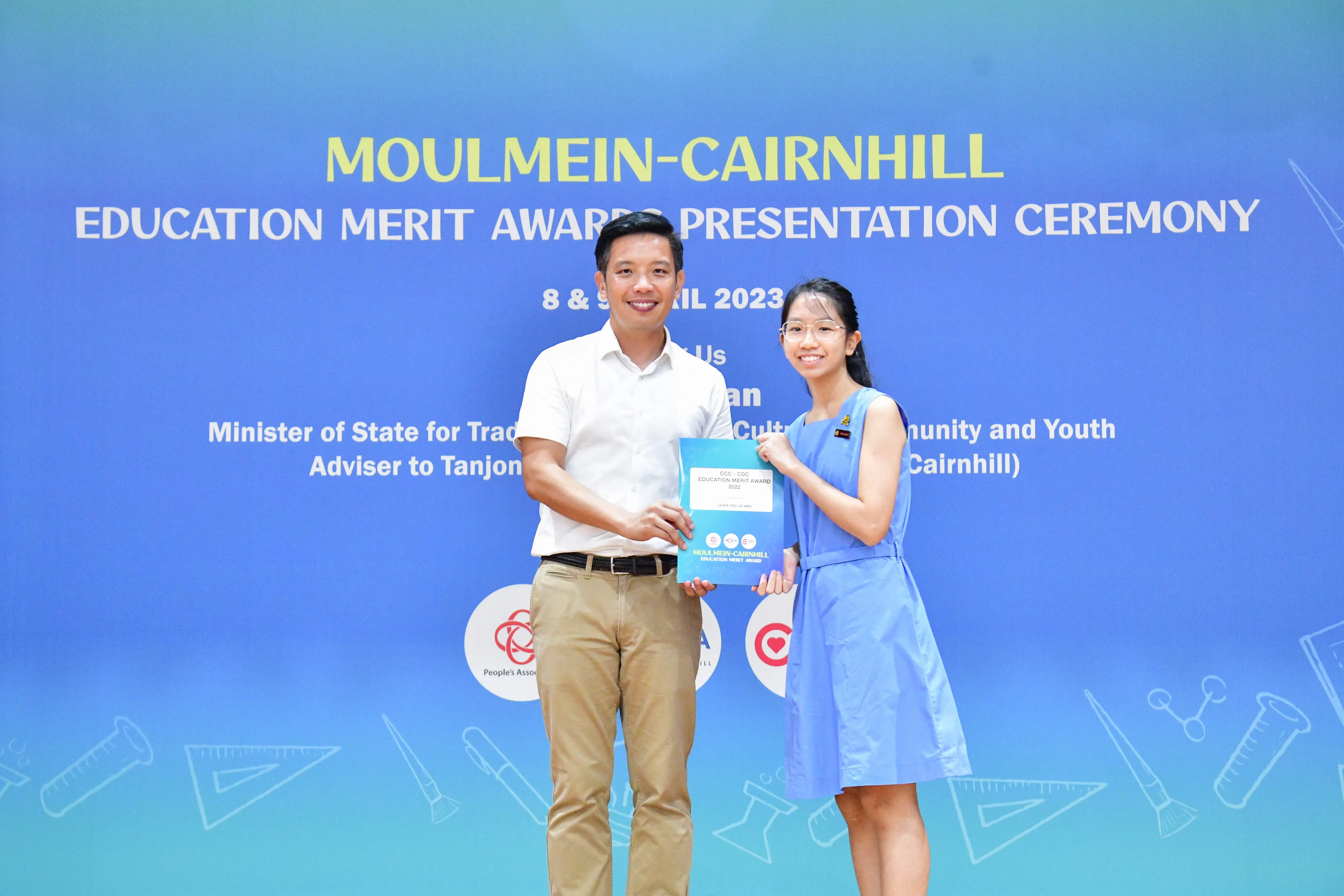 Two people smile while holding an award booklet at the Moulmein-Cairnhill Education Merit Awards Ceremony 2023.