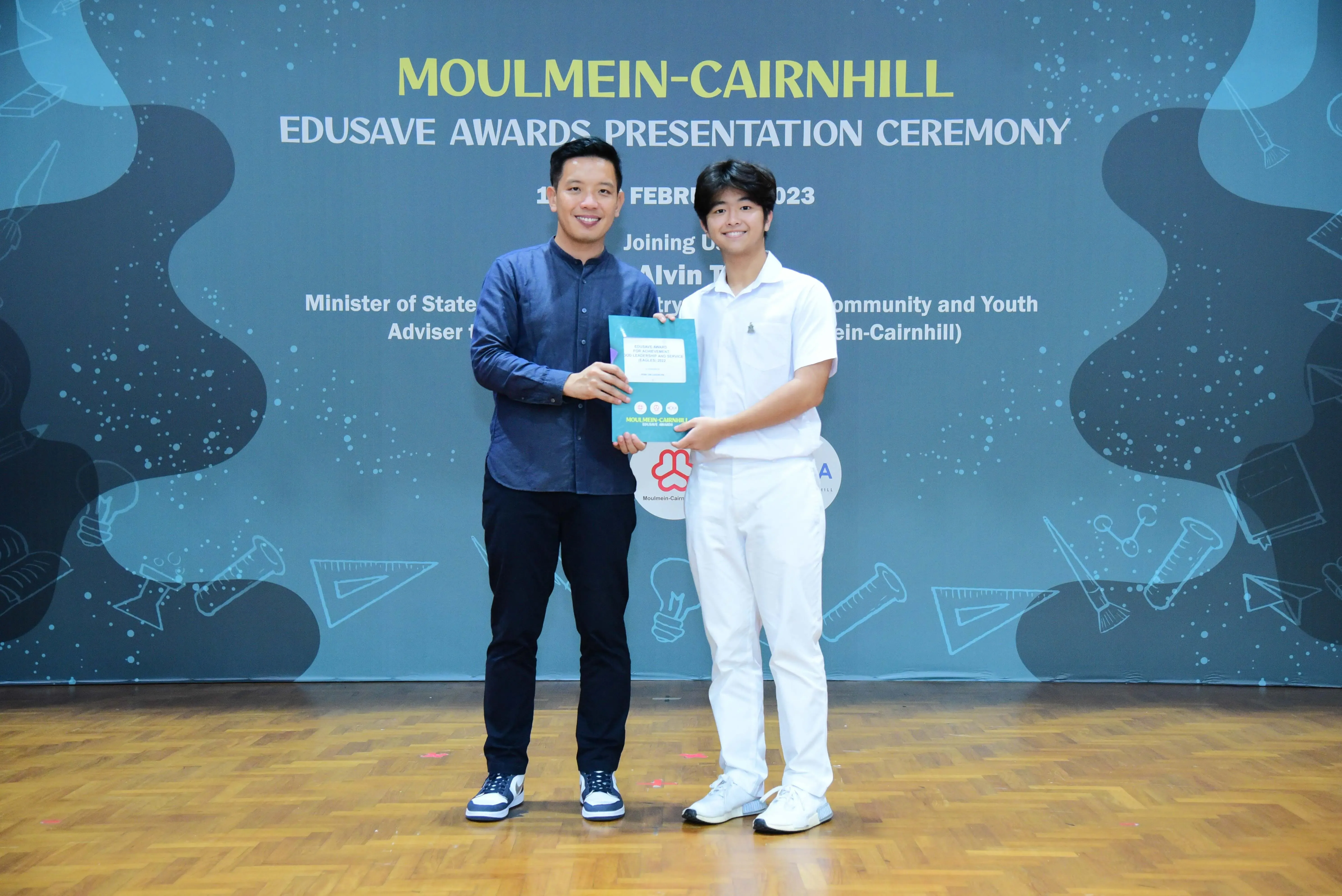 Two men hold a certificate together at the Moulmein-Cairnhill Edusave Awards Presentation Ceremony in February 2023.