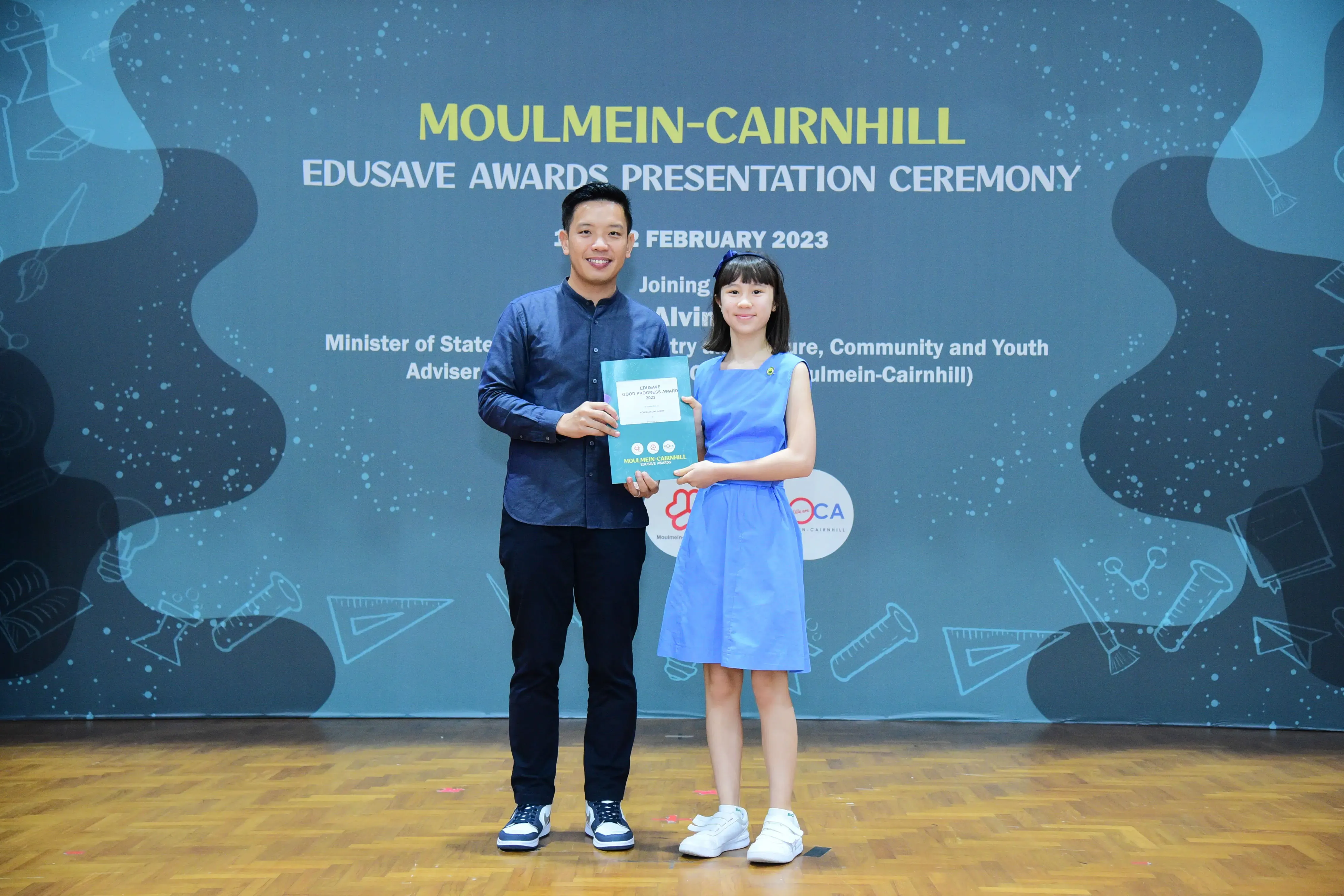 A man and a young girl hold a certificate at the Moulmein-Cairnhill Edusave Awards Presentation Ceremony, February 2023.