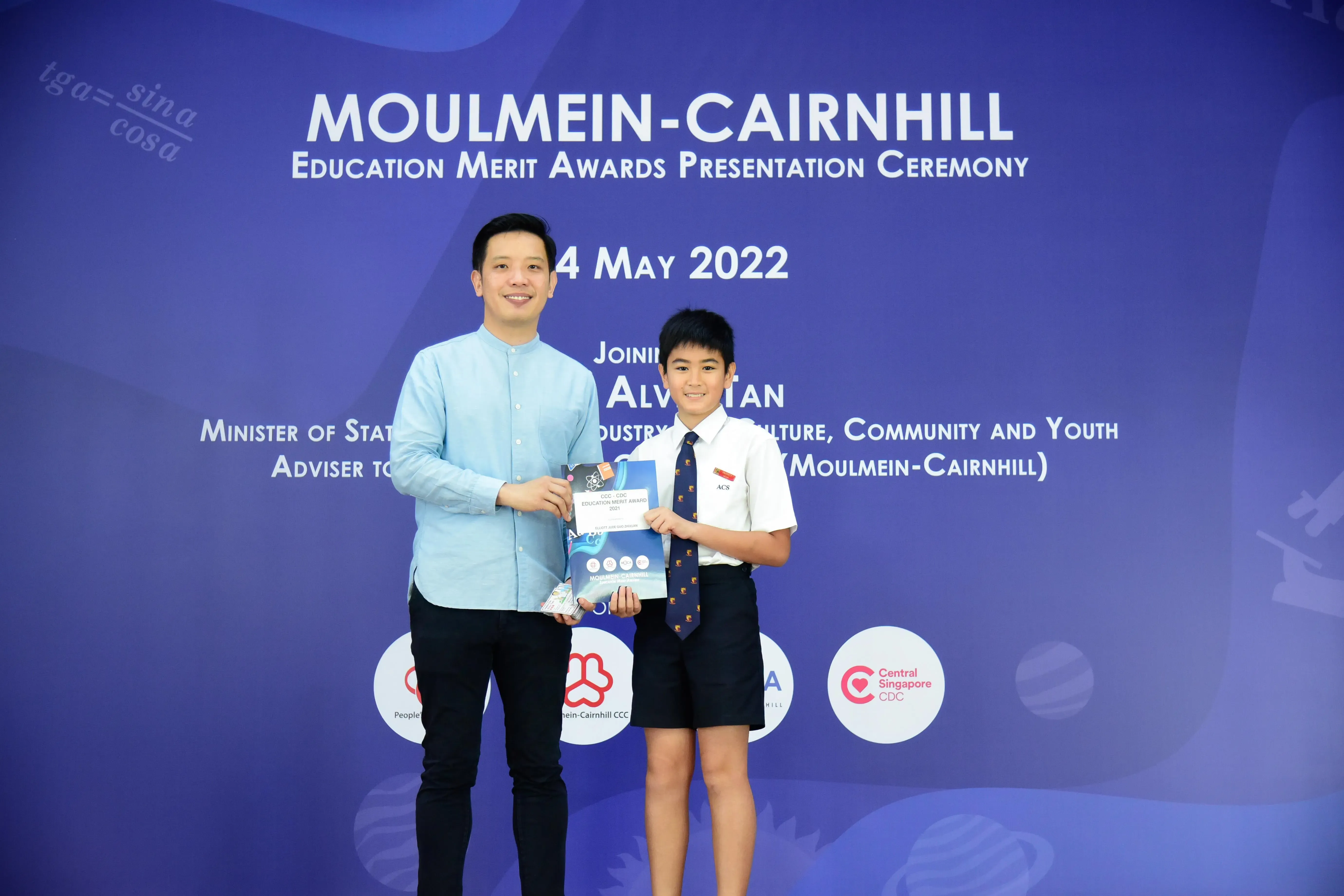 A man and a young boy in school uniform hold an award at the Moulmein-Cairnhill Education Merit Awards ceremony, May 2022.
