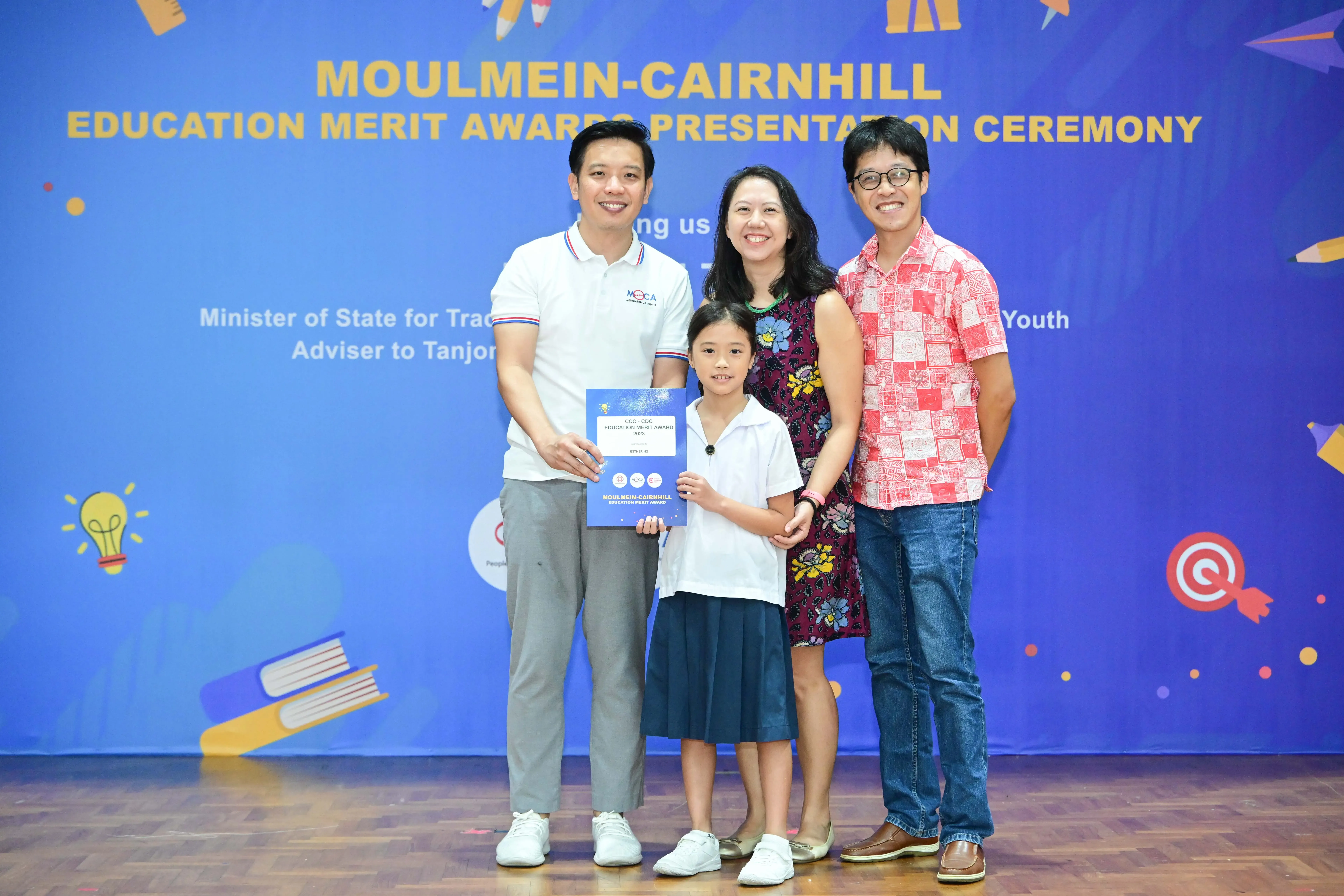 Three adults and a young girl holding a certificate pose at the Moulmein-Cairnhill Education Merit Awards Ceremony.