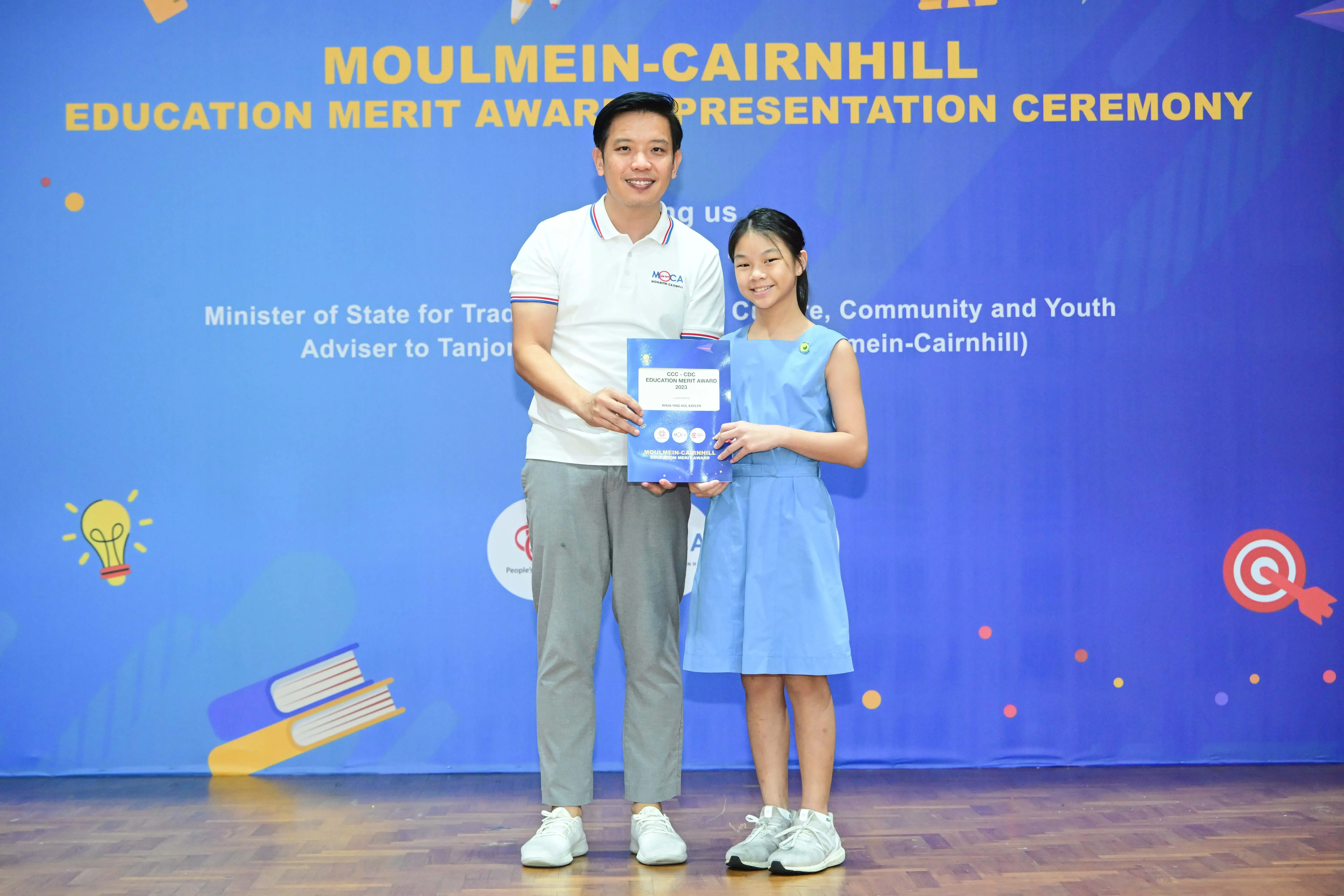 A man and a young girl hold an award certificate at the Moulmein-Cairnhill Education Merit Award Presentation Ceremony.