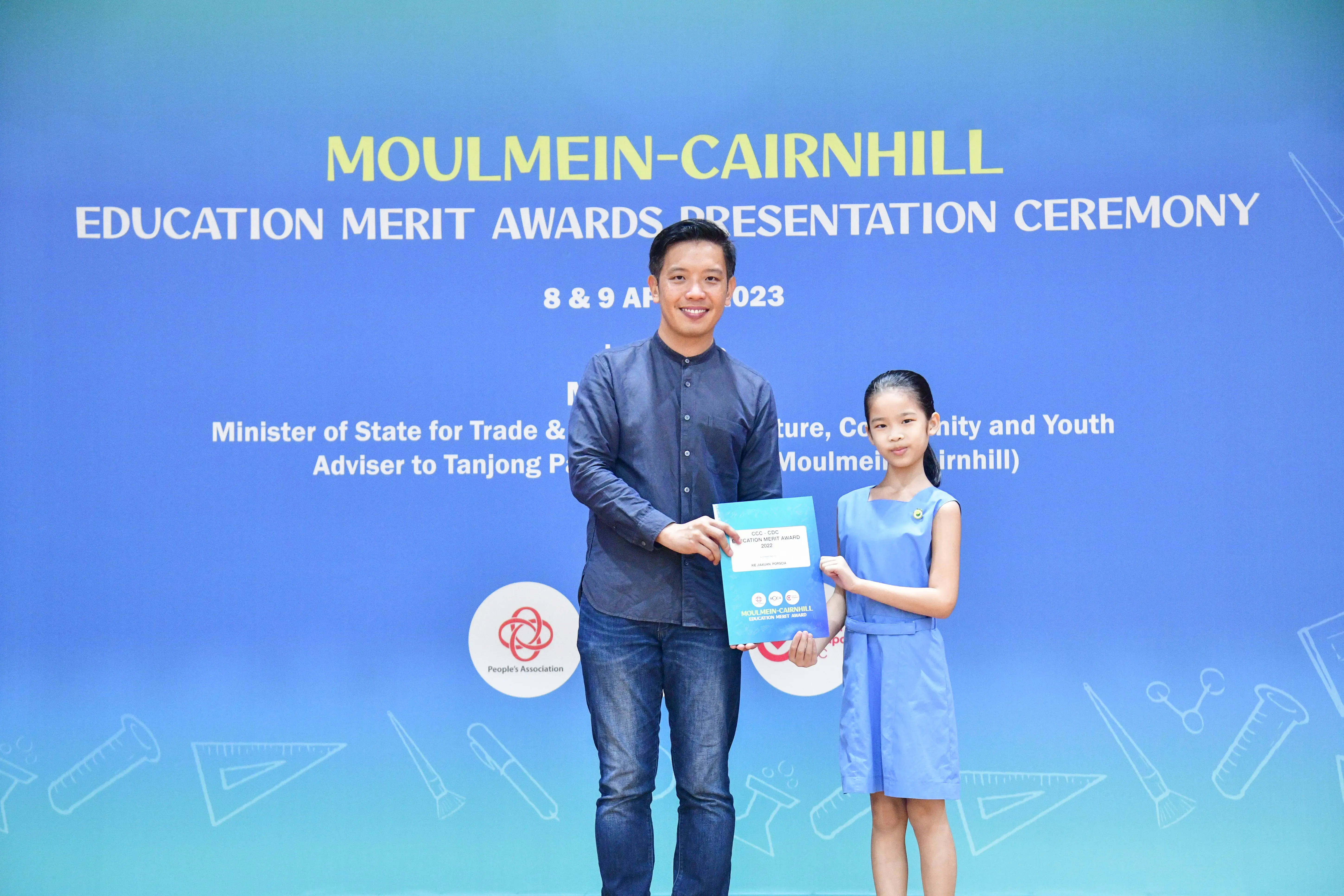 A man and a young girl hold an award certificate at the Moulmein-Cairnhill Education Merit Awards Ceremony, April 2023.