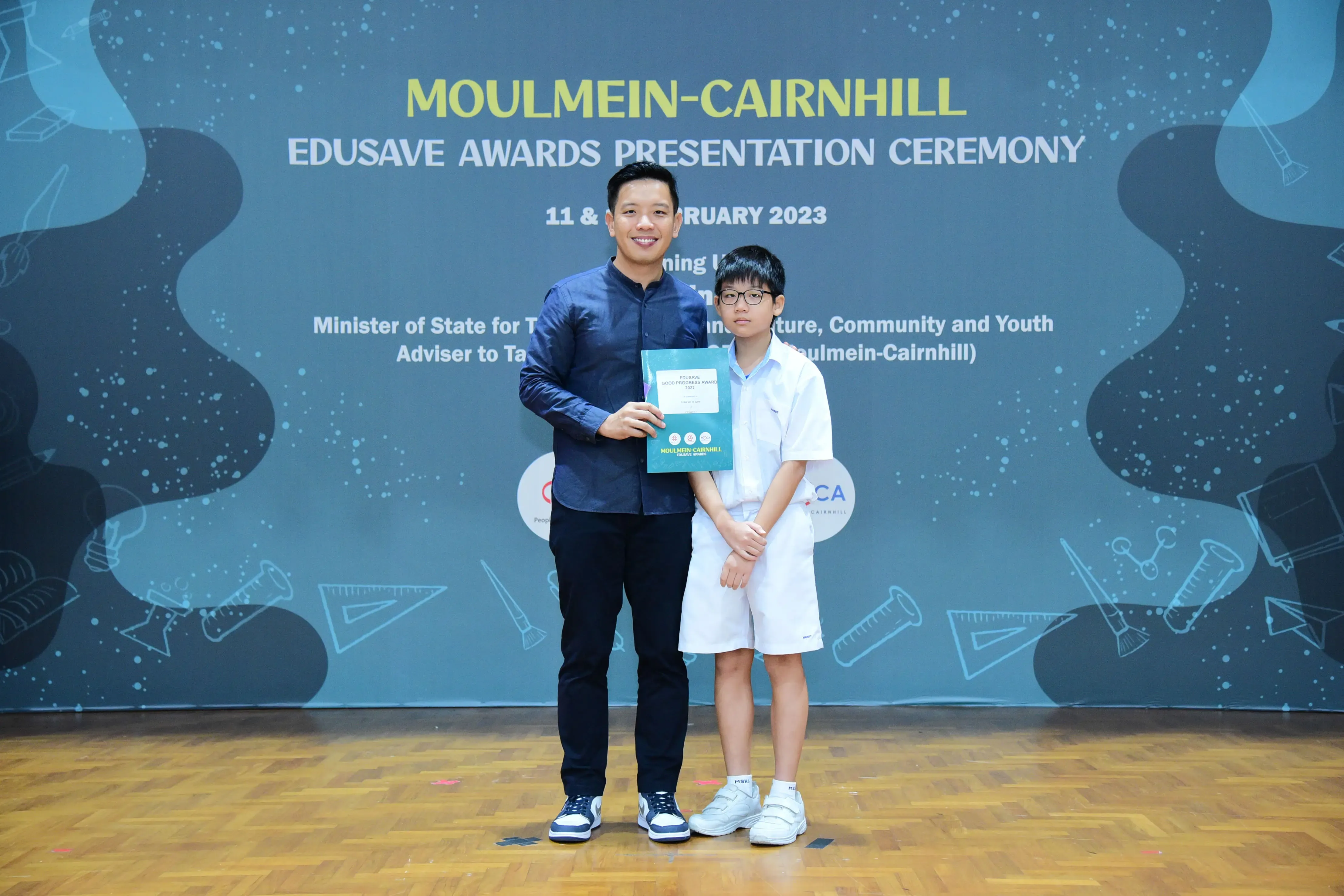 An adult and a young student pose together holding an award at the Moulmein-Cairnhill Edusave Awards Ceremony 2023.