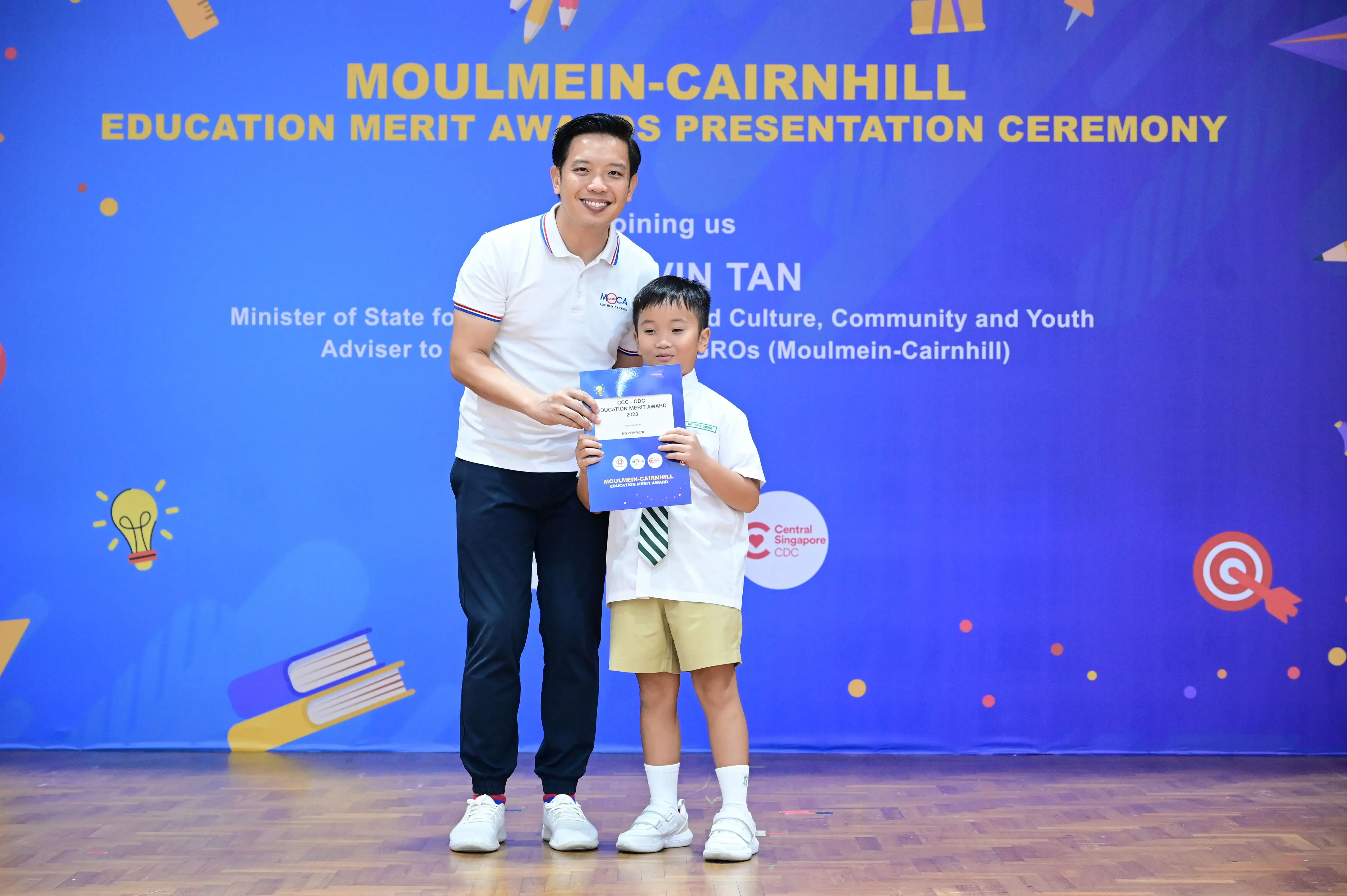 A man and a young boy hold a certificate at the Moulmein-Cairnhill Education Merit Awards Presentation Ceremony.