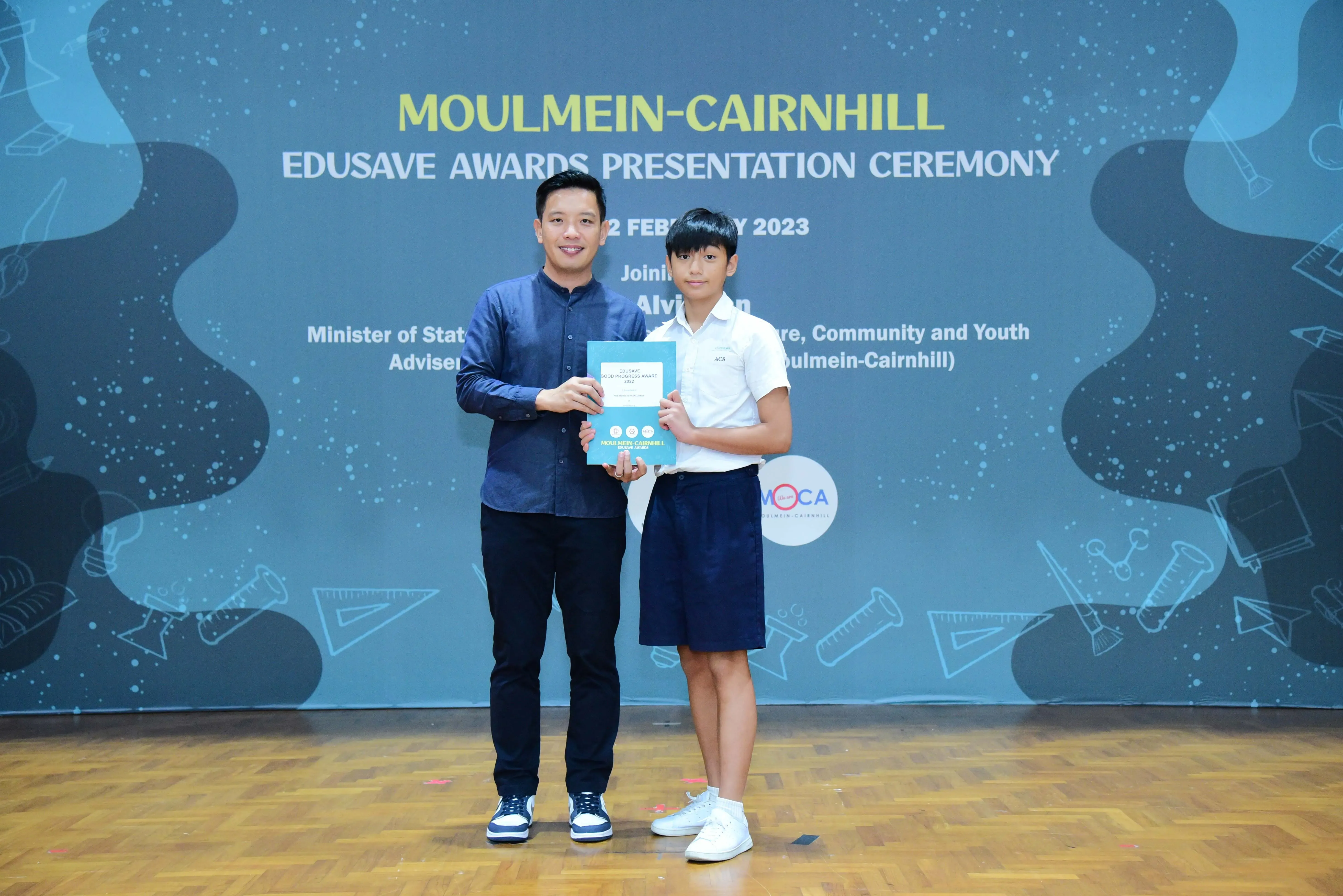 An adult and a young student hold a certificate at the Moulmein-Cairnhill Edusave Awards Ceremony in 2023.