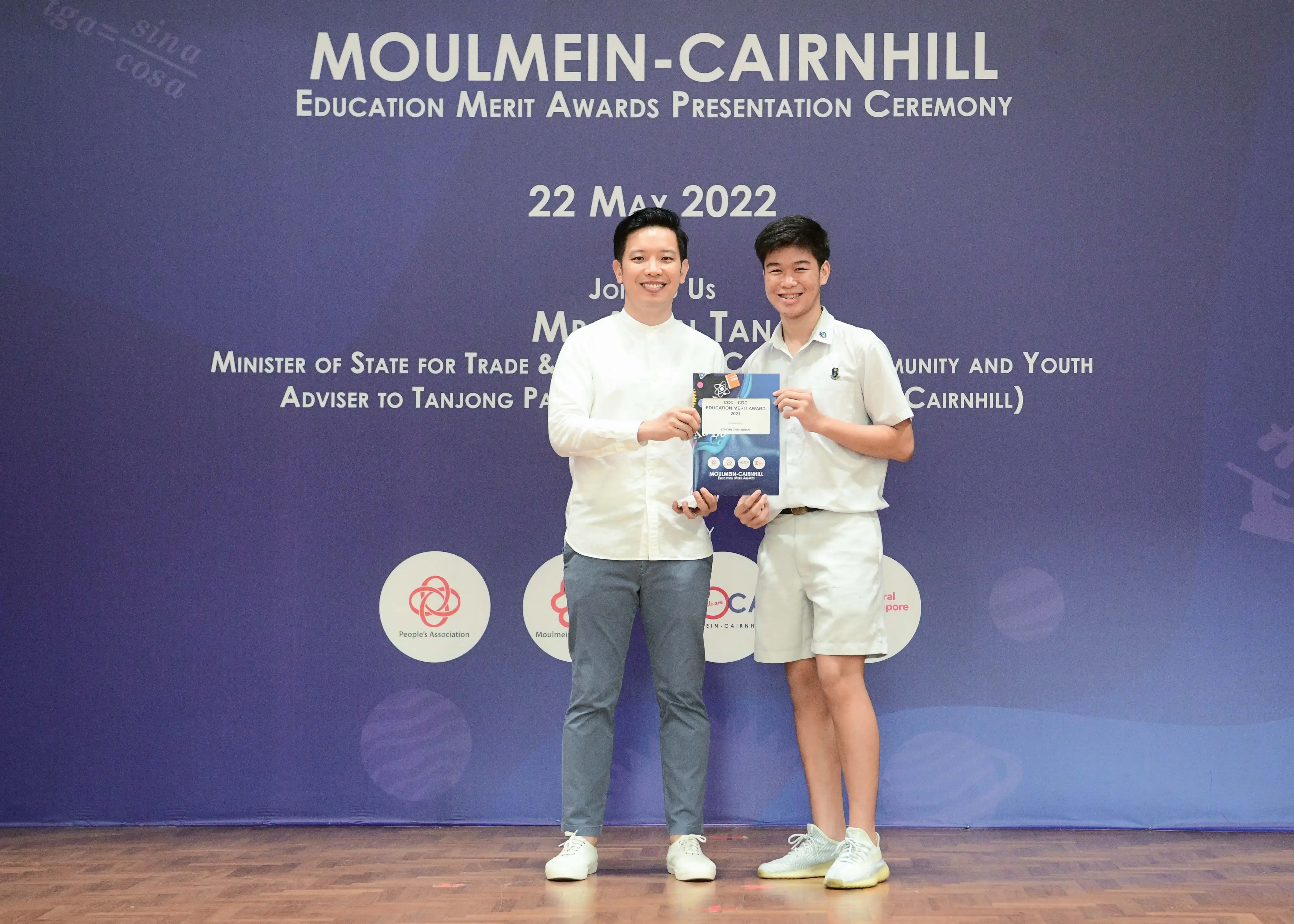 Two men pose holding an award booklet at the Moulmein-Cairnhill Education Merit Awards Ceremony on 22 May 2022.