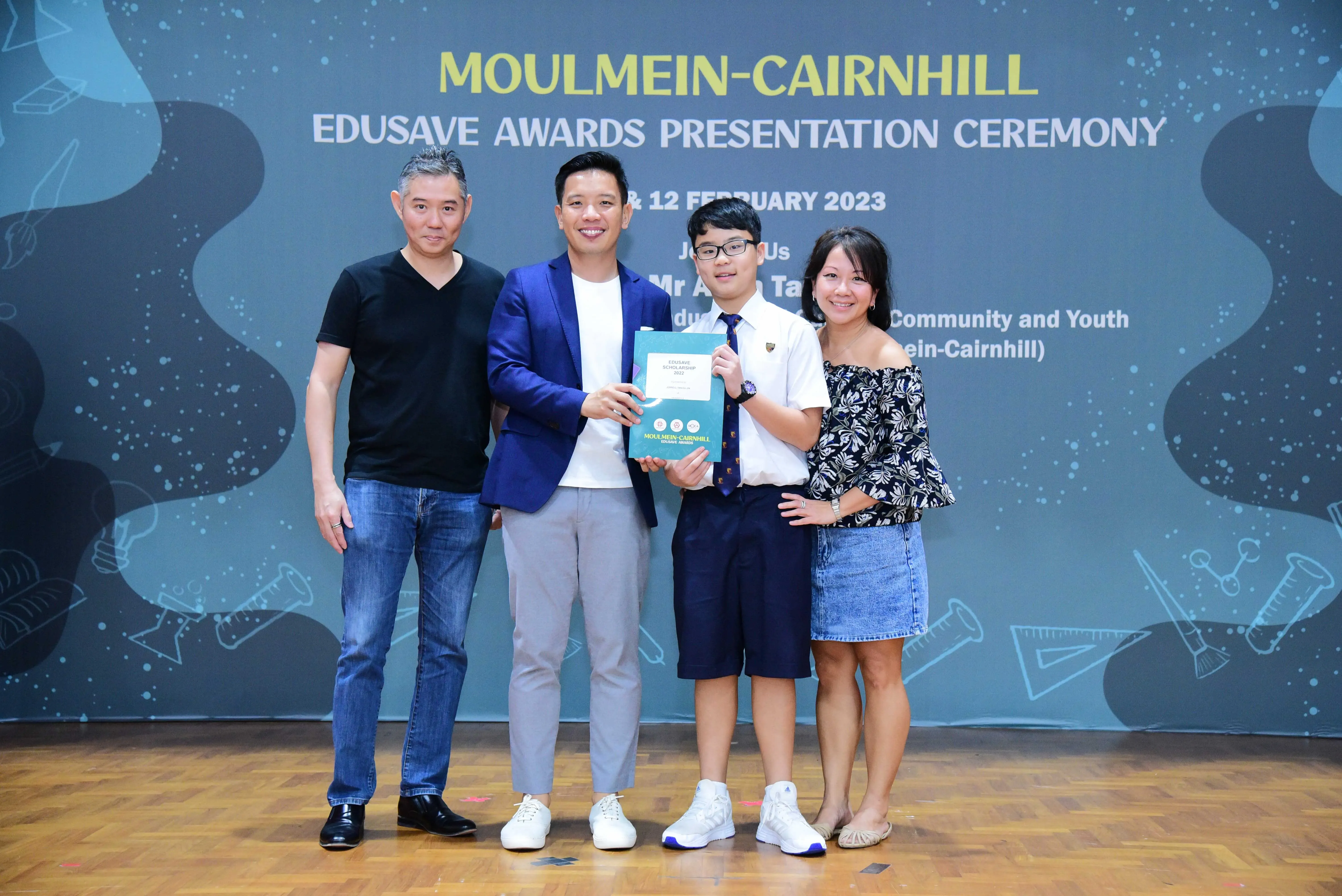 Four people pose at the Moulmein-Cairnhill Edusave Awards Presentation Ceremony, with a student holding a certificate.