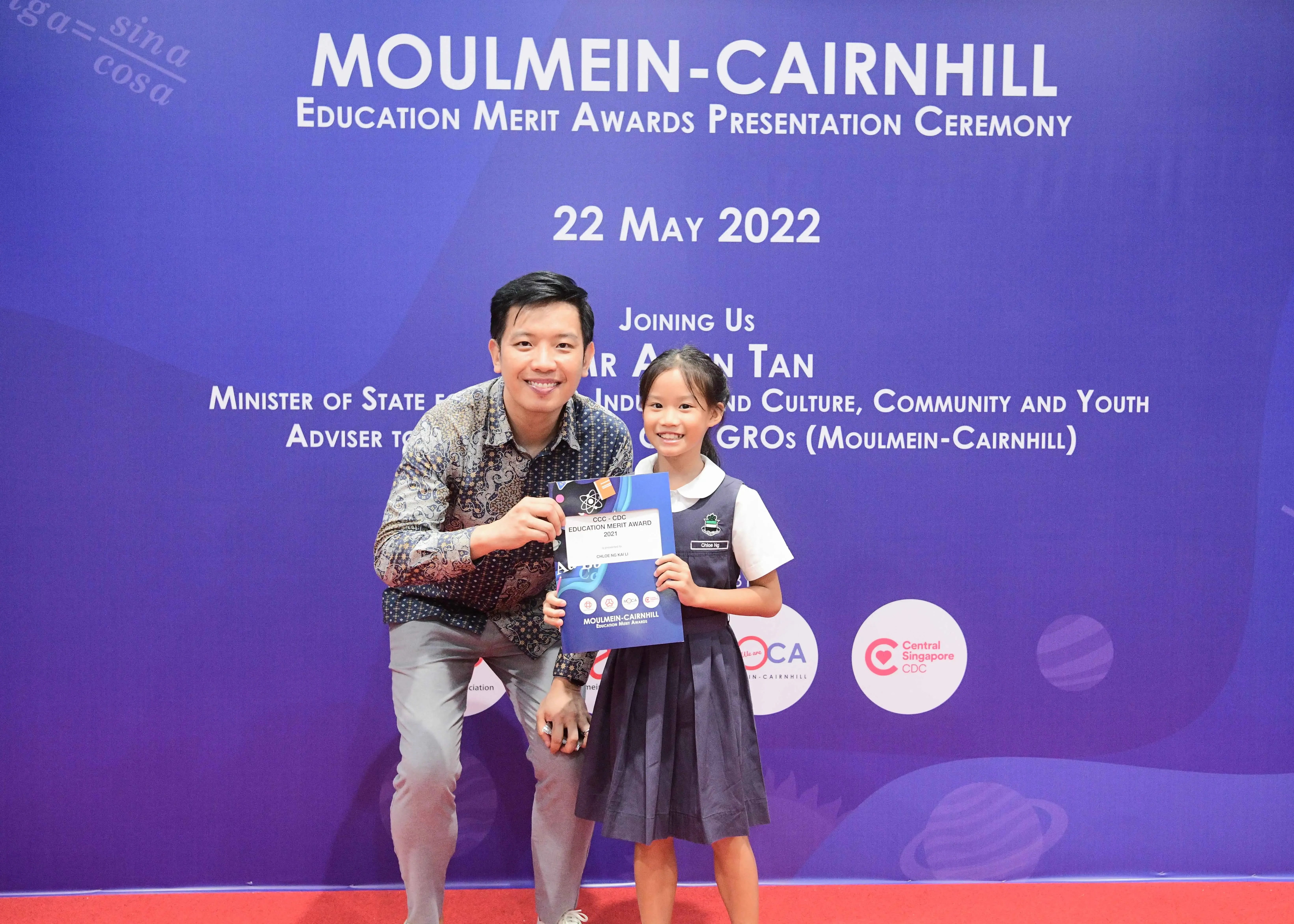 A man and a young girl in school uniform hold an award certificate at the Moulmein-Cairnhill Education Merit Awards 2022.