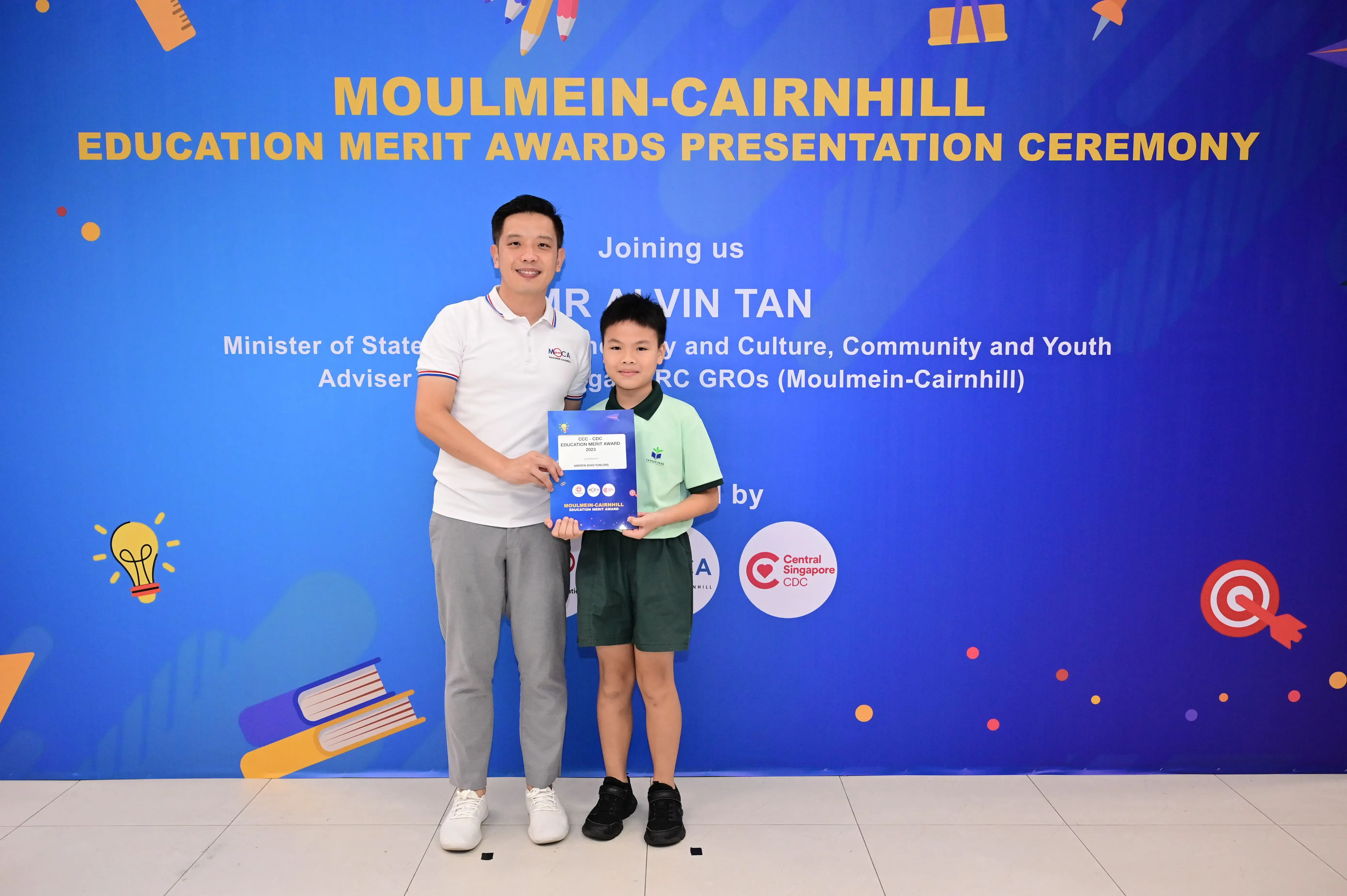 A man and a young boy hold an award certificate at the Moulmein-Cairnhill Education Merit Awards Presentation Ceremony.