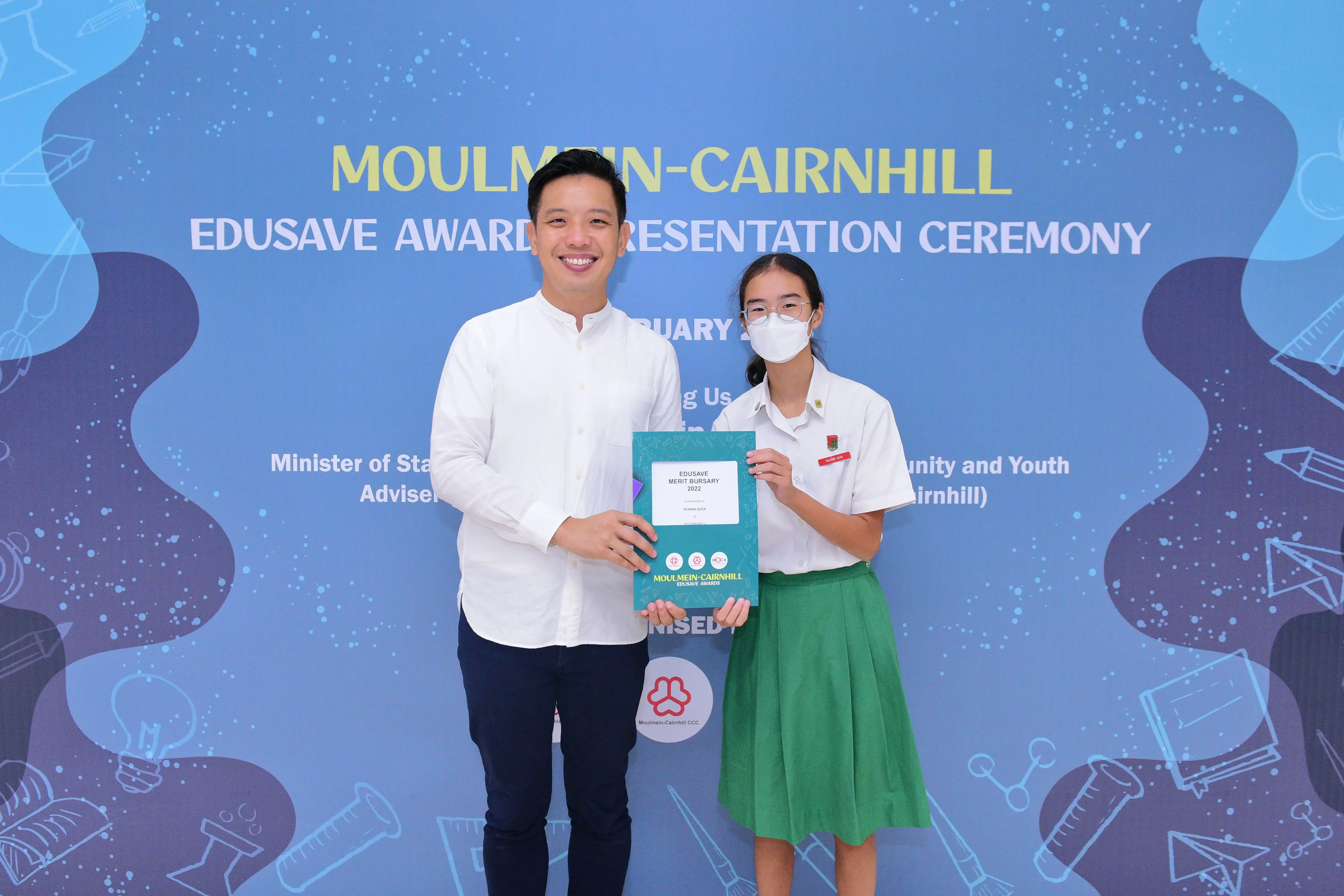 Two people hold an Edusave Merit Bursary 2022 certificate at the Moulmein-Cairnhill Edusave Awards Ceremony.