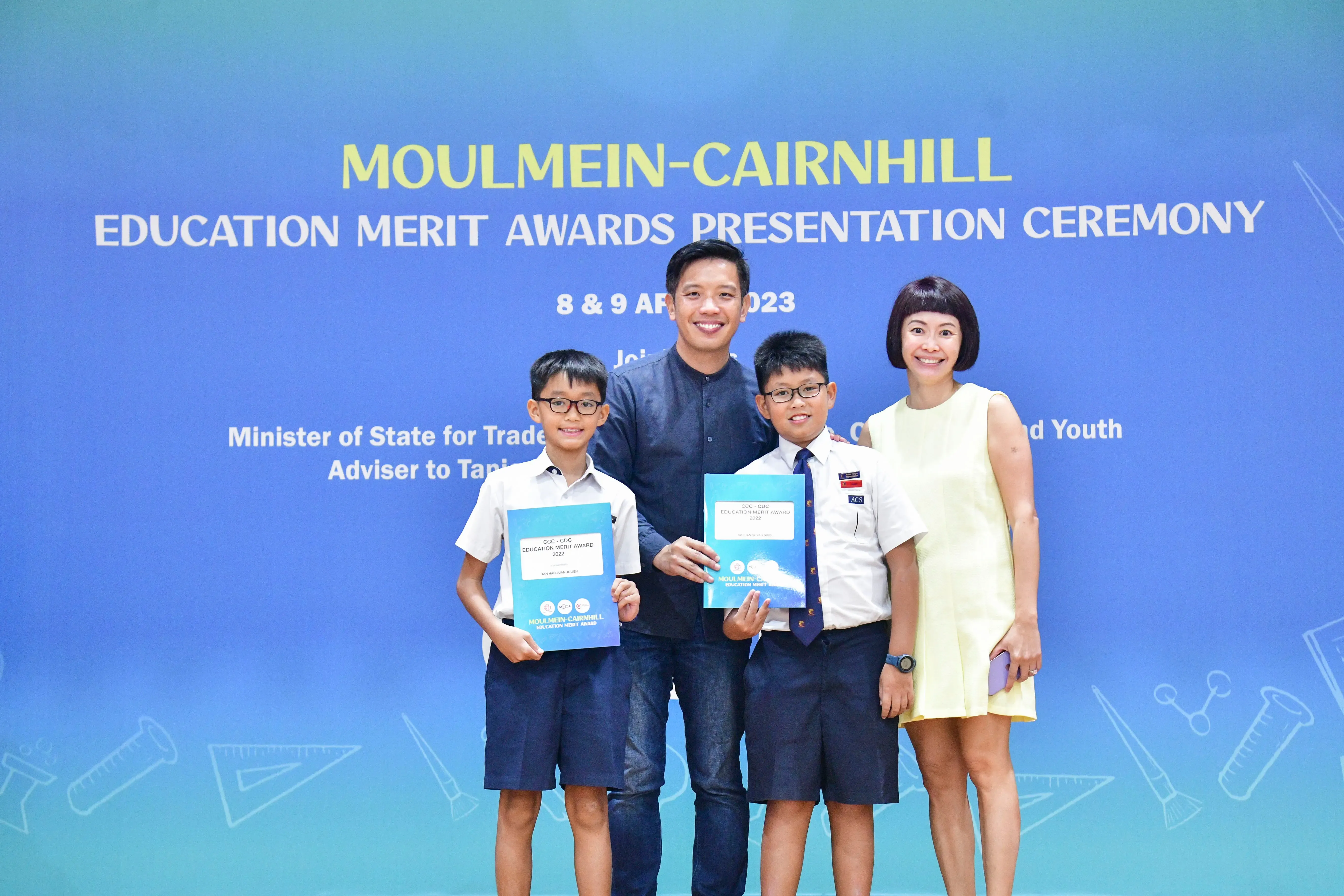 Two adults and two boys holding award folders pose at the Moulmein-Cairnhill Education Merit Awards Ceremony, April 2023.