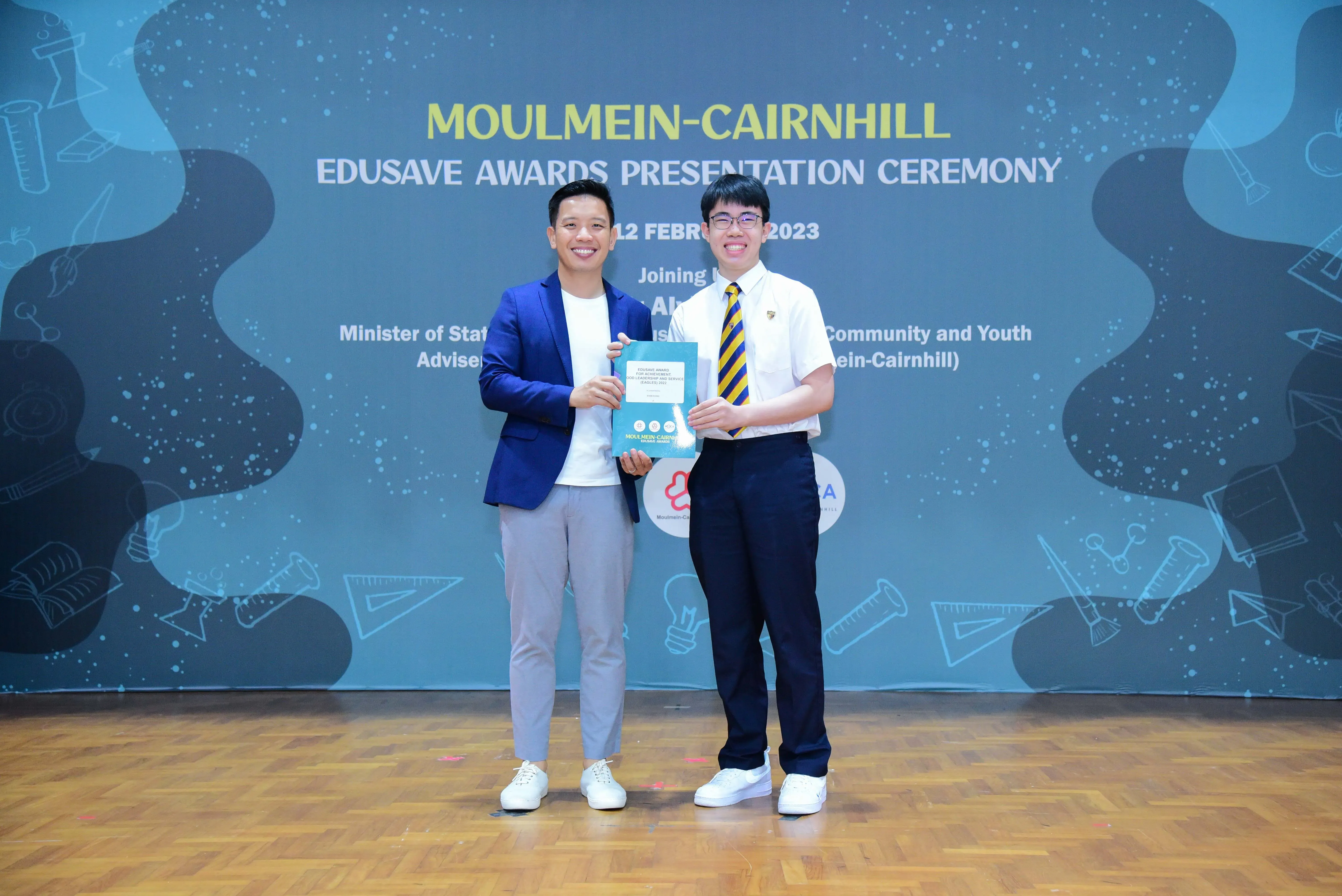 Two men smile holding a certificate at the Moulmein-Cairnhill Edusave Awards Presentation Ceremony on 12 February 2023.