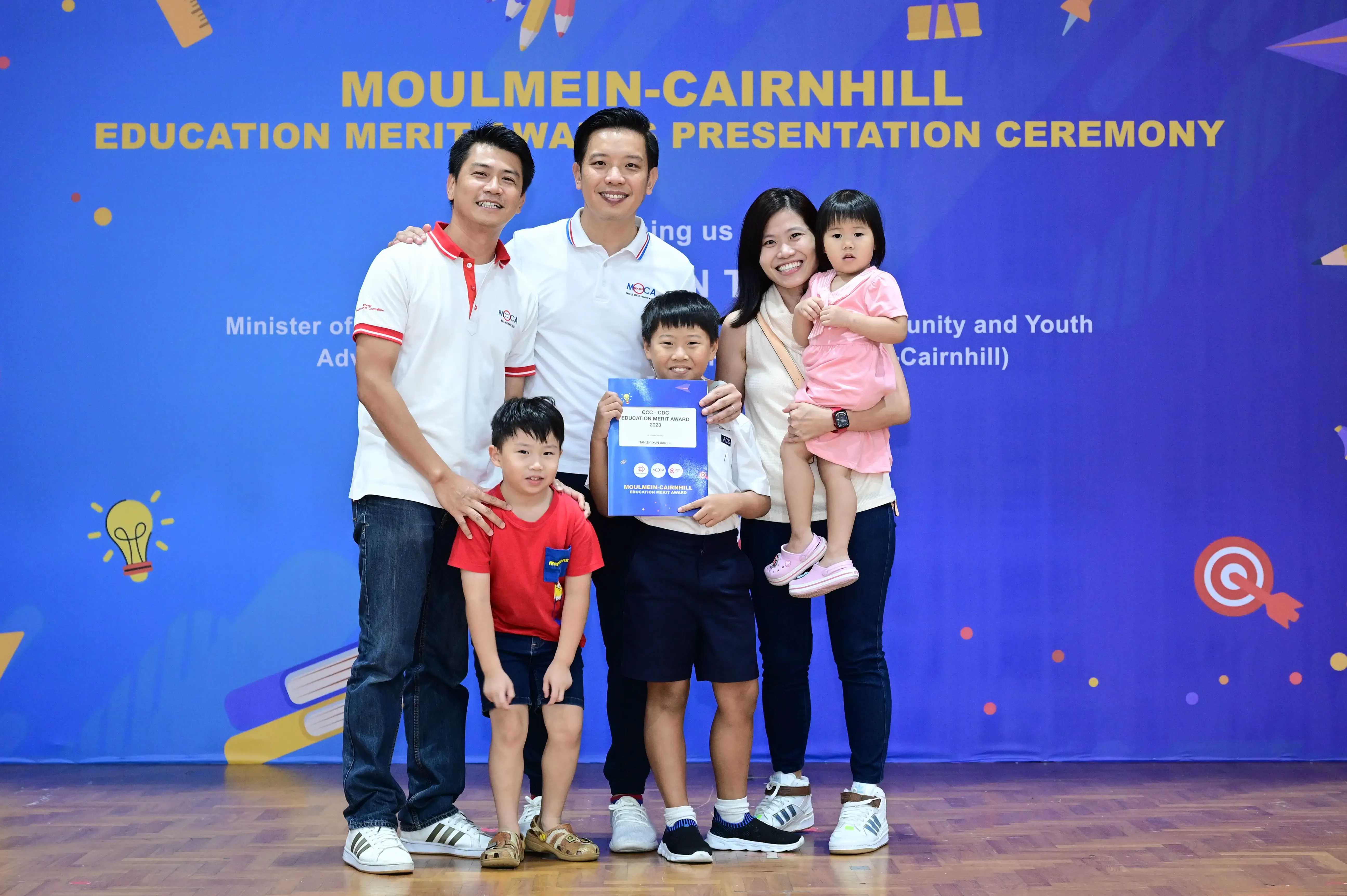 A family of five poses with a boy holding an award certificate at the Moulmein-Cairnhill Education Merit Awards Ceremony.