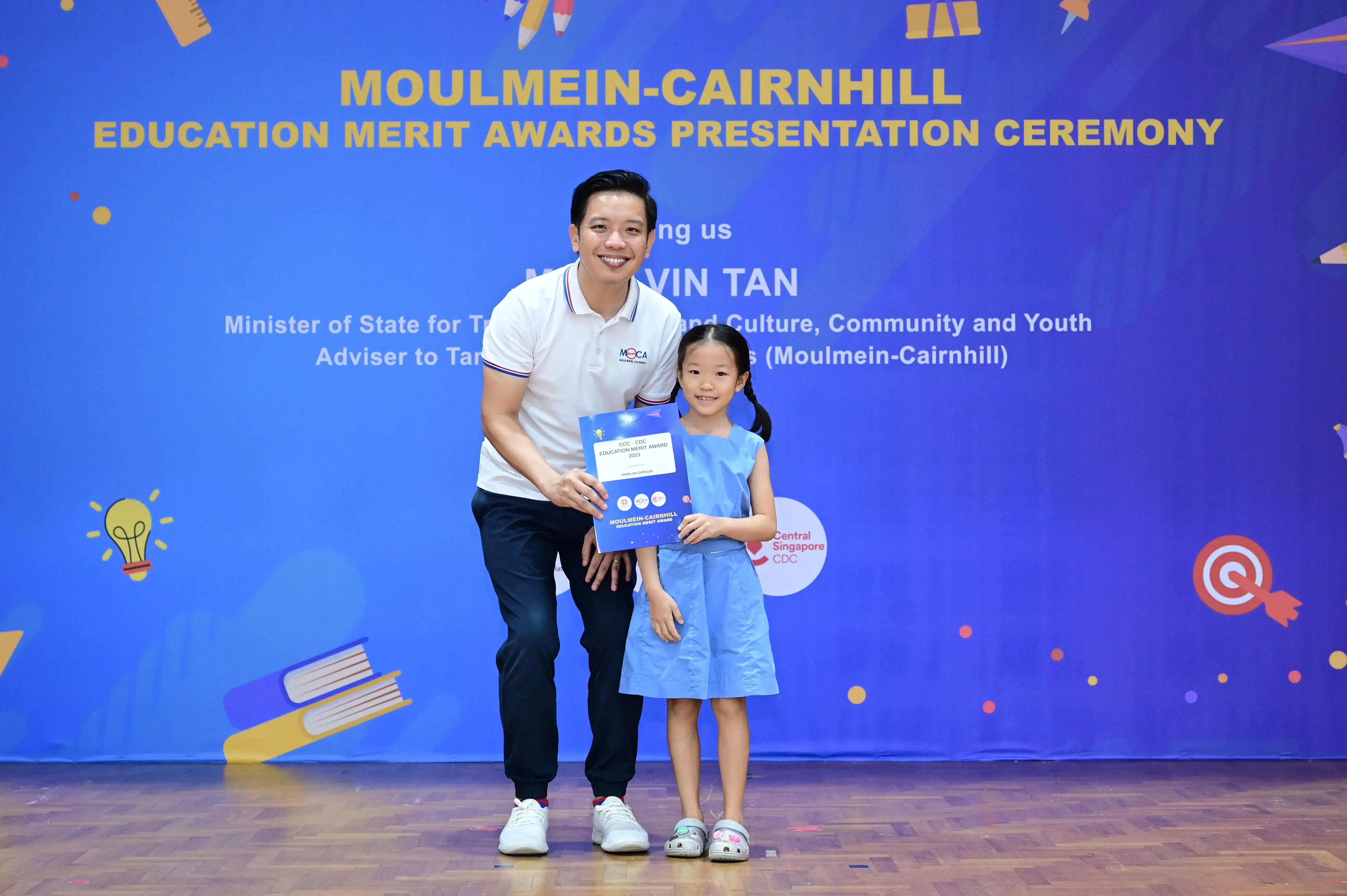 A man and a young girl hold a certificate at the Moulmein-Cairnhill Education Merit Awards Presentation Ceremony.