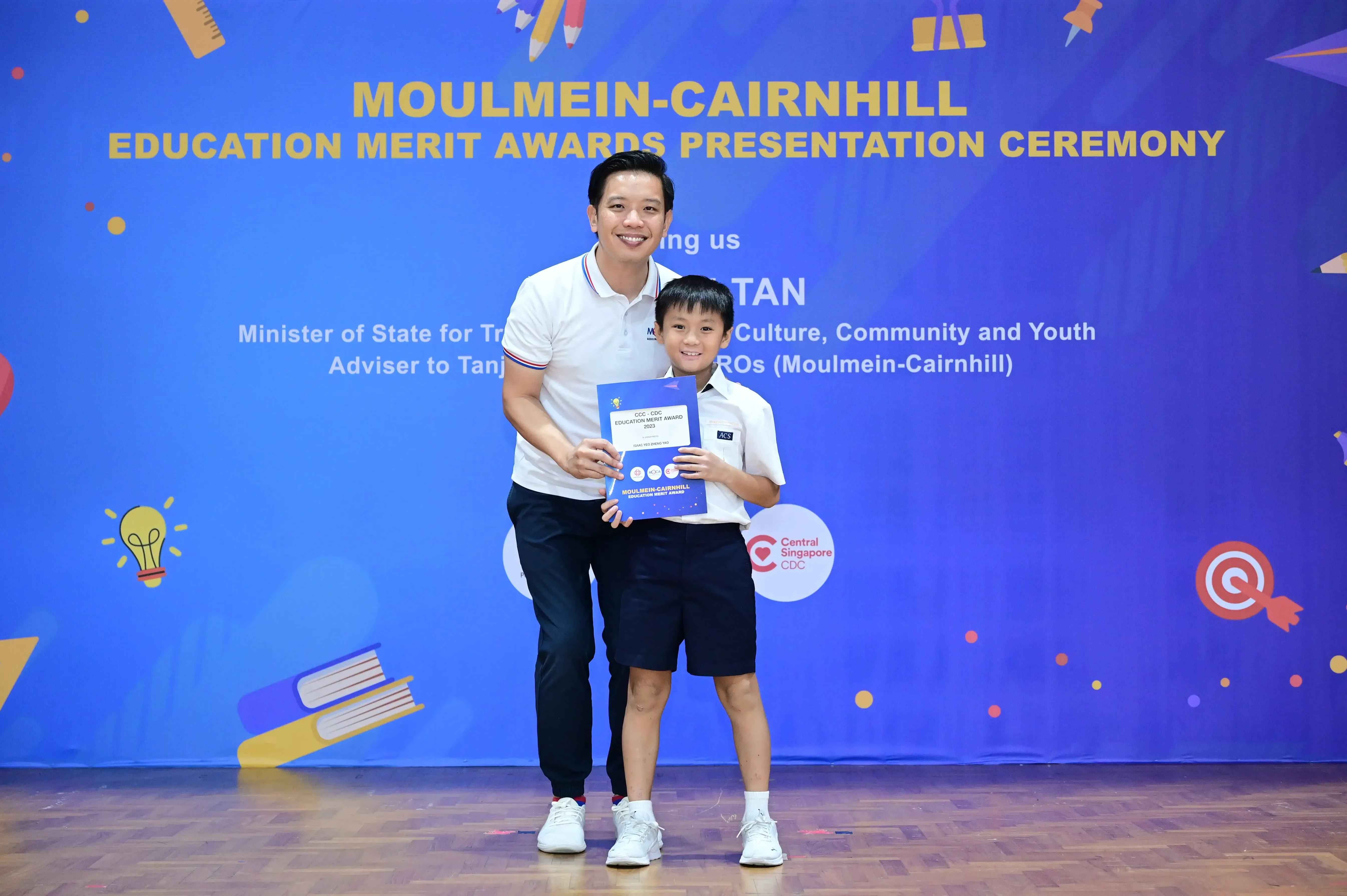 A man and a young boy hold an award certificate at the Moulmein-Cairnhill Education Merit Awards Presentation Ceremony.