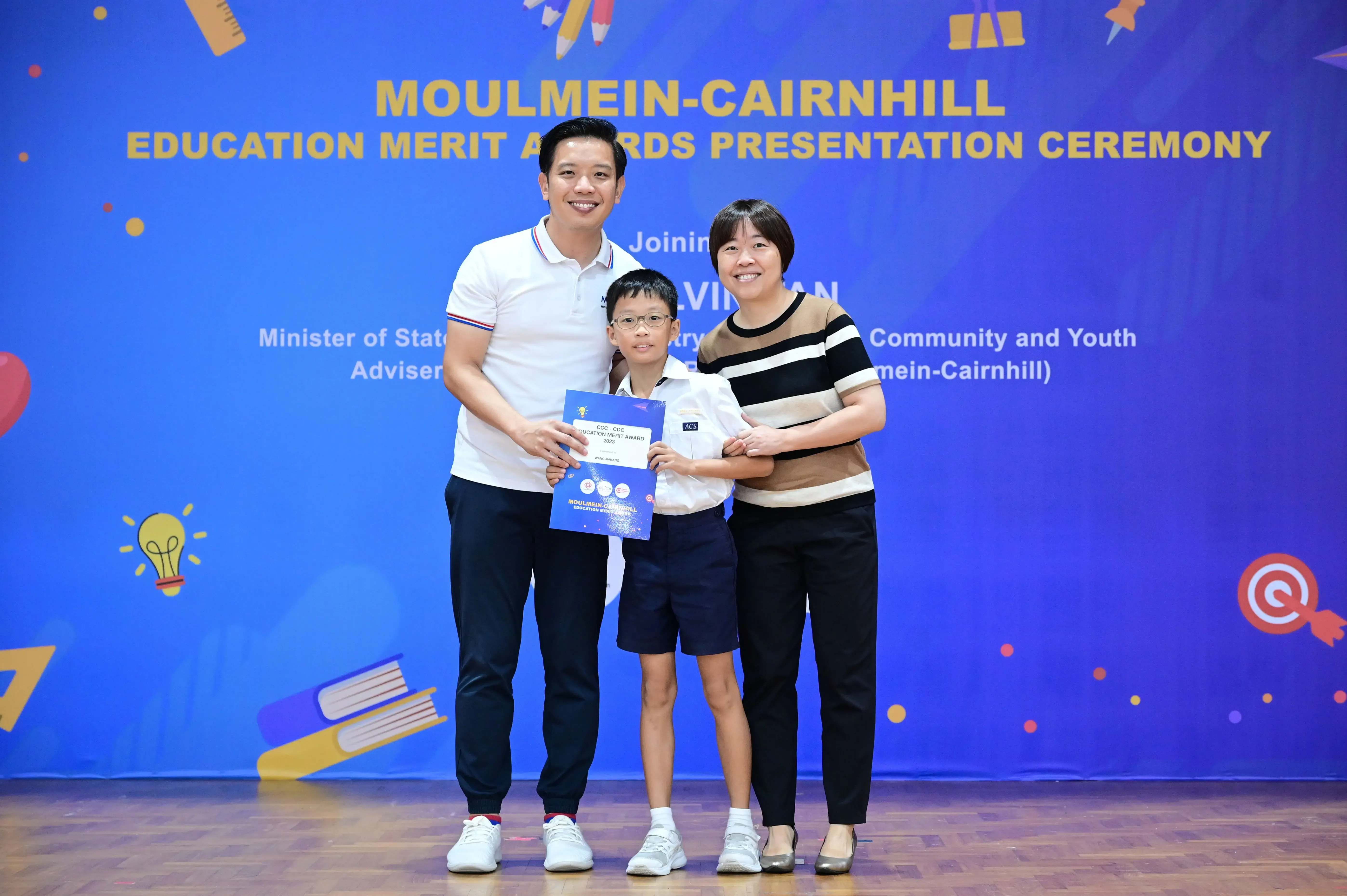 Two adults and a young boy holding certificates at the Moulmein-Cairnhill Education Merit Awards Presentation Ceremony.