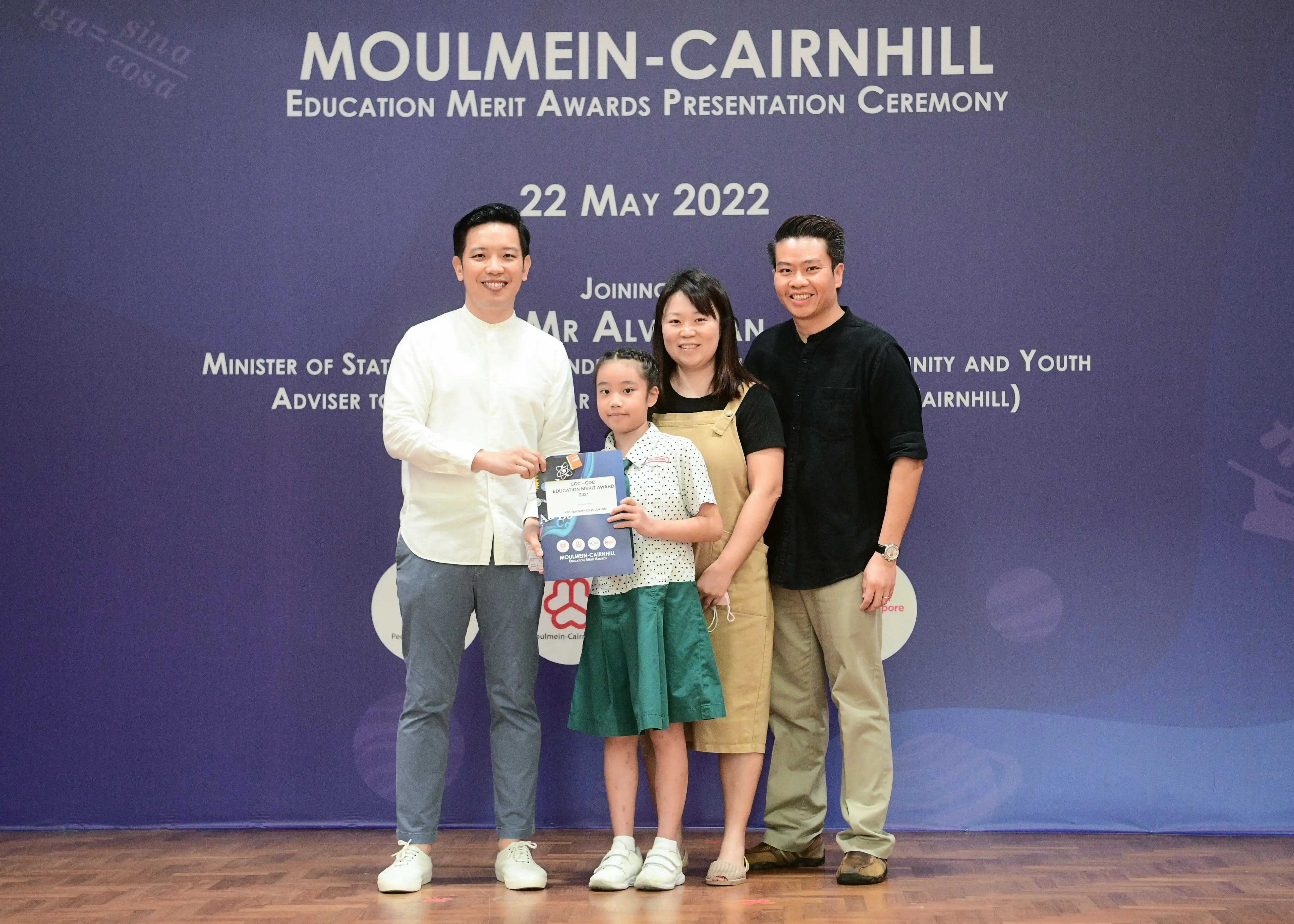 Four people pose at the Moulmein-Cairnhill Education Merit Awards ceremony on 22 May 2022, with a girl holding an award certificate.