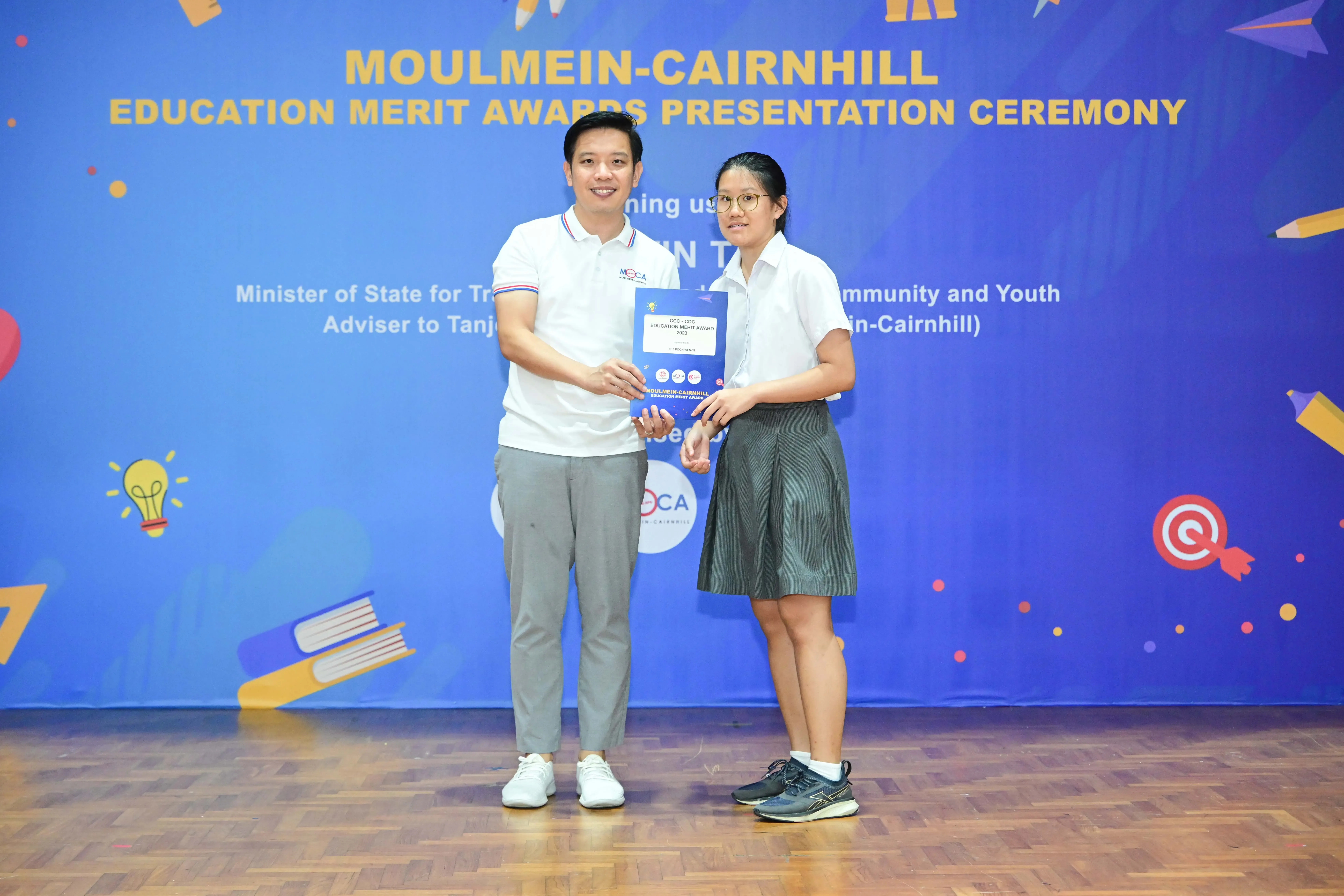 Two people hold an award certificate at the Moulmein-Cairnhill Education Merit Awards Presentation Ceremony.