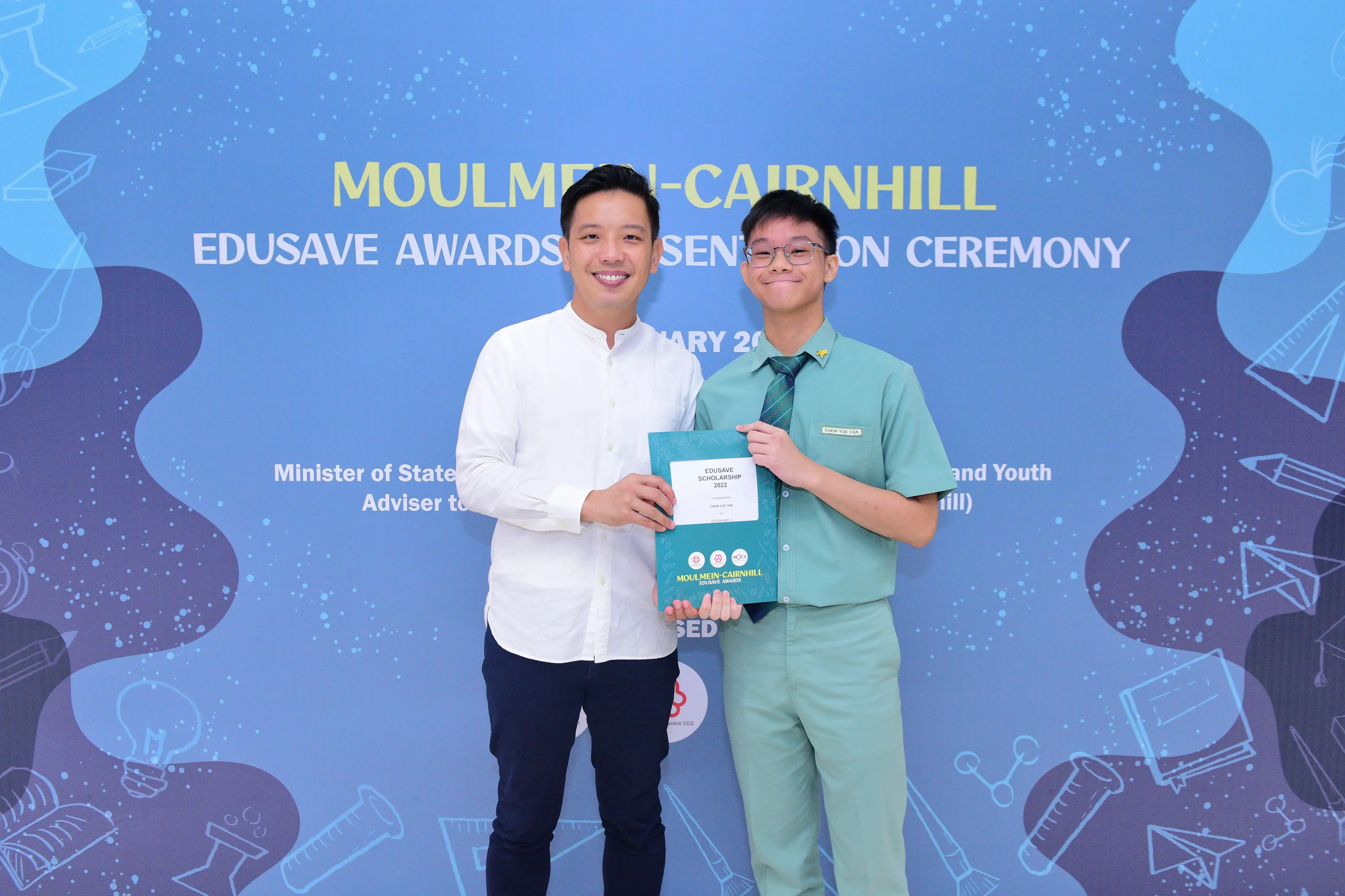 Two people smile holding an Edusave Scholarship certificate at the Moulmein-Cairnhill Edusave Awards Presentation Ceremony.