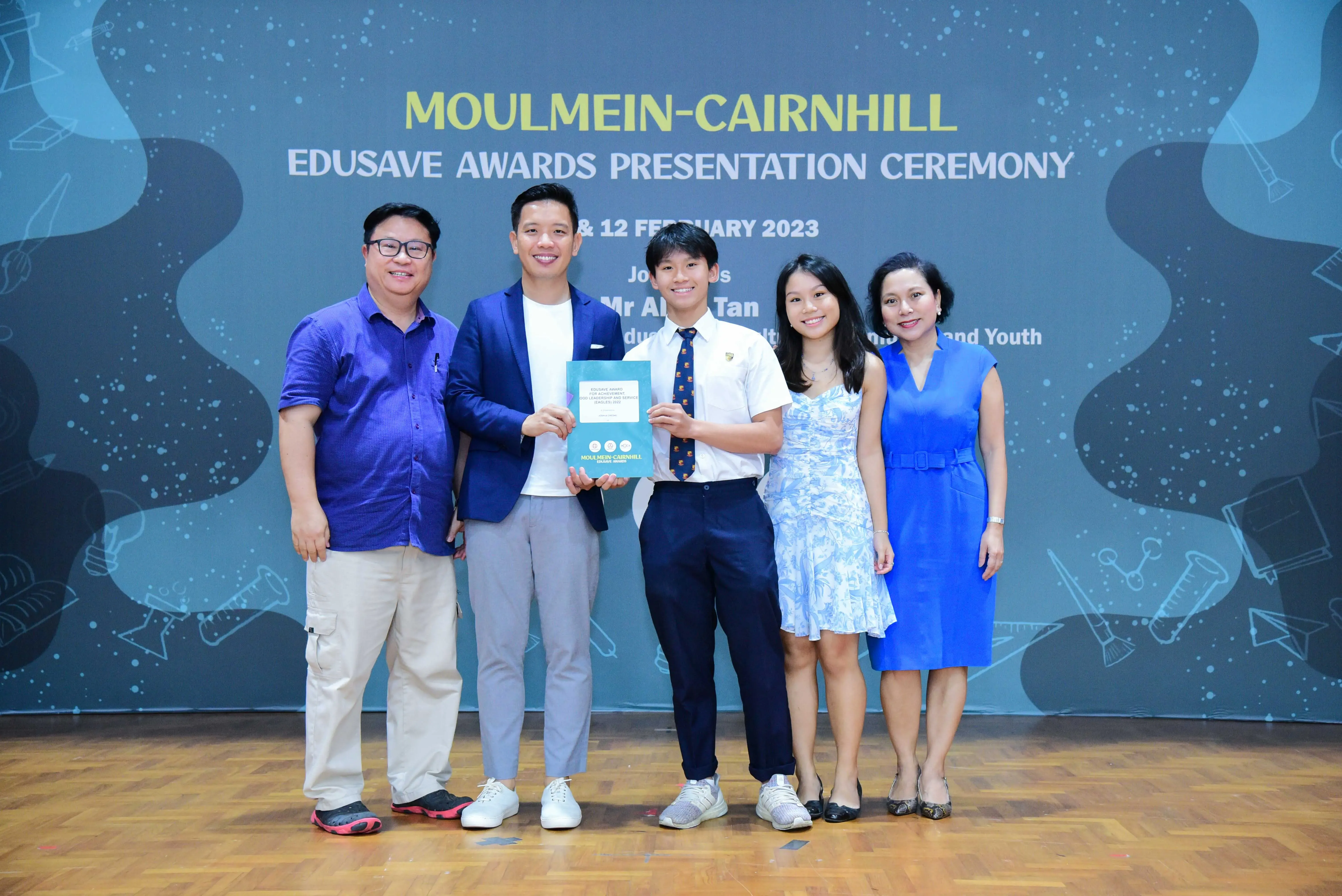 Five people pose on a stage at the Moulmein-Cairnhill Edusave Awards Presentation Ceremony, February 2023.