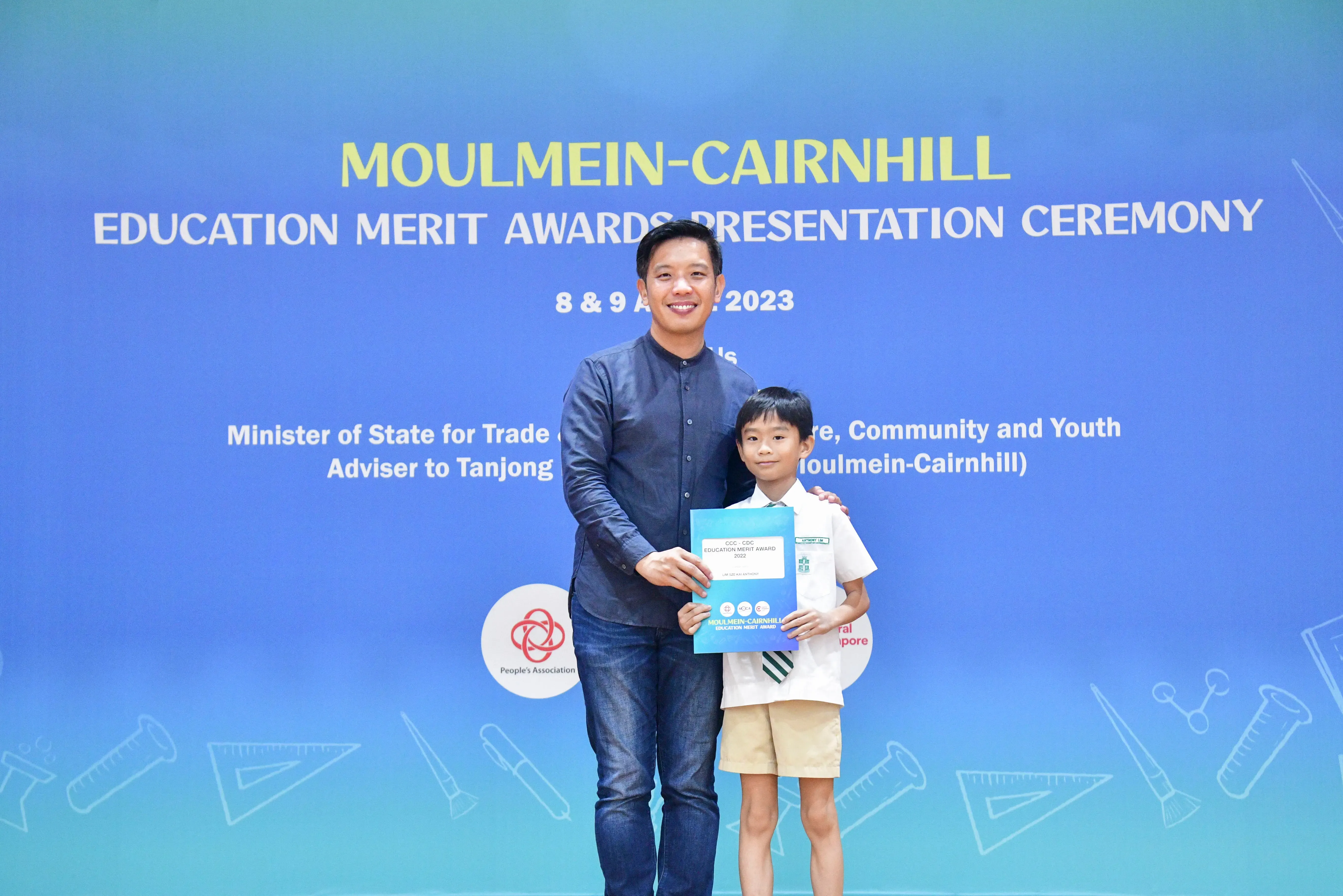 A man and a young boy hold an award certificate at the Moulmein-Cairnhill Education Merit Awards Ceremony 2023.