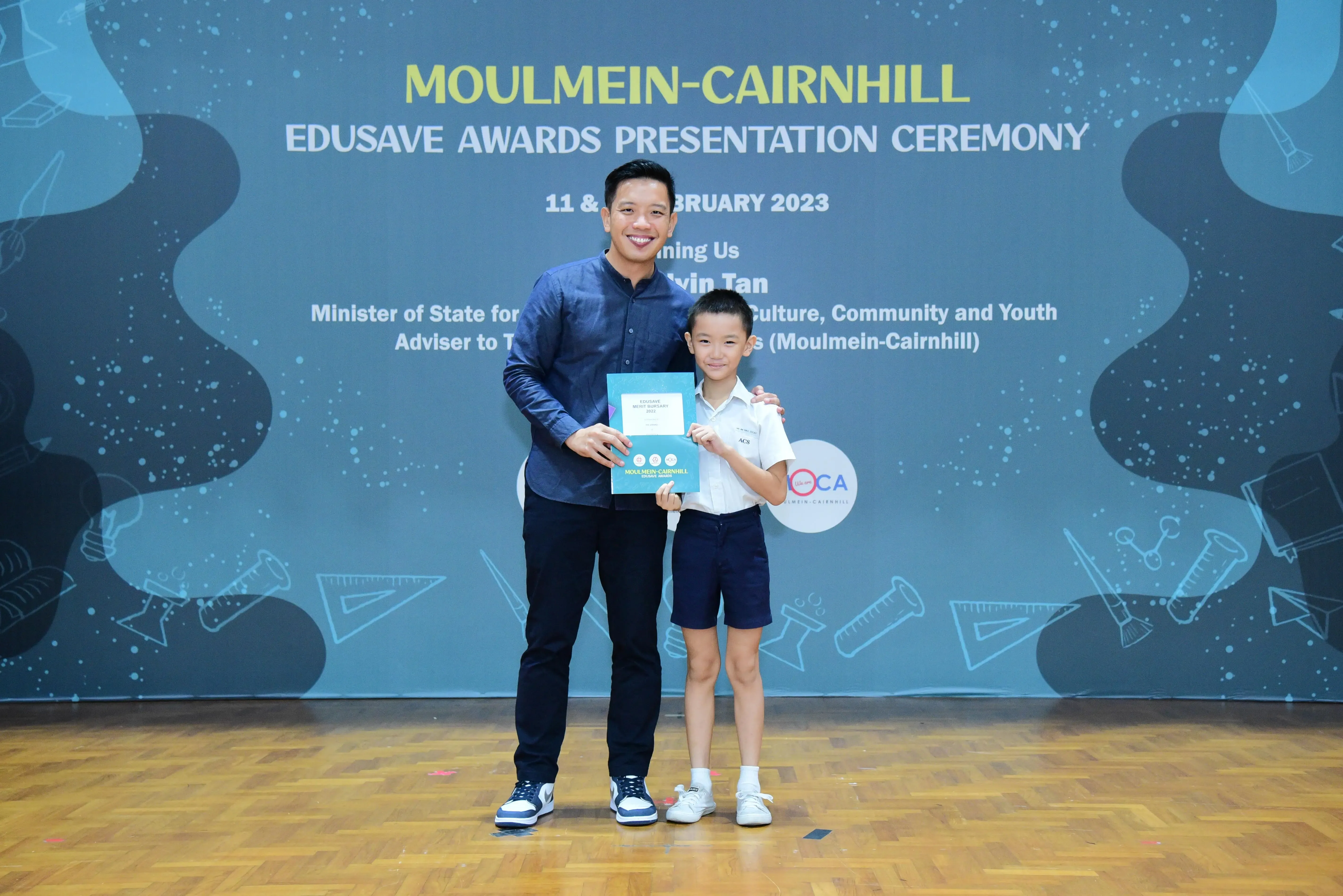 A man and a young boy hold a certificate at the Moulmein-Cairnhill Edusave Awards Presentation Ceremony 2023.