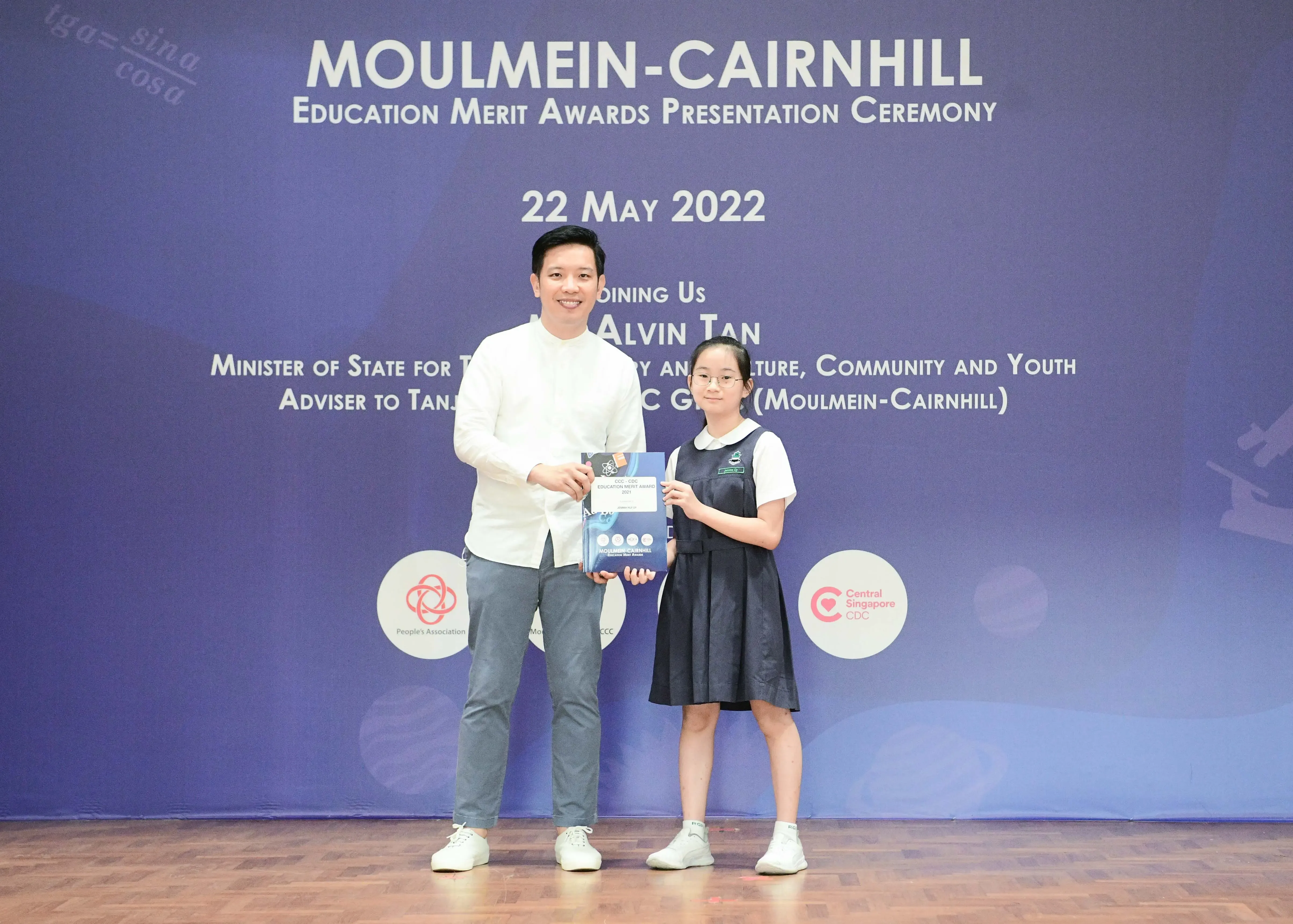 A man and a young girl in school uniform hold an award at the Moulmein-Cairnhill Education Merit Awards ceremony on 22 May 2022.
