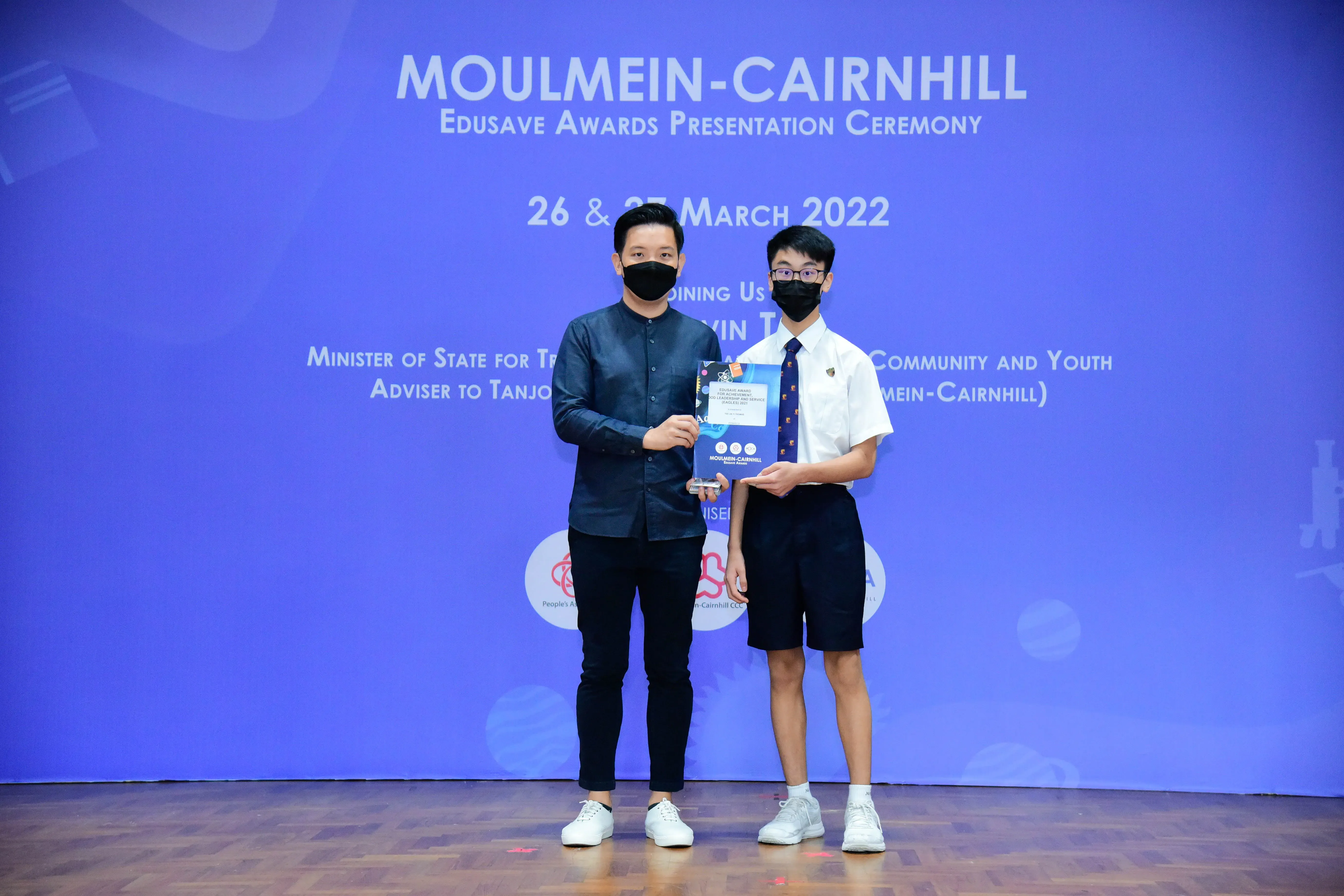 Two masked individuals hold an award at the Moulmein-Cairnhill Edusave Awards Presentation Ceremony, March 2022.