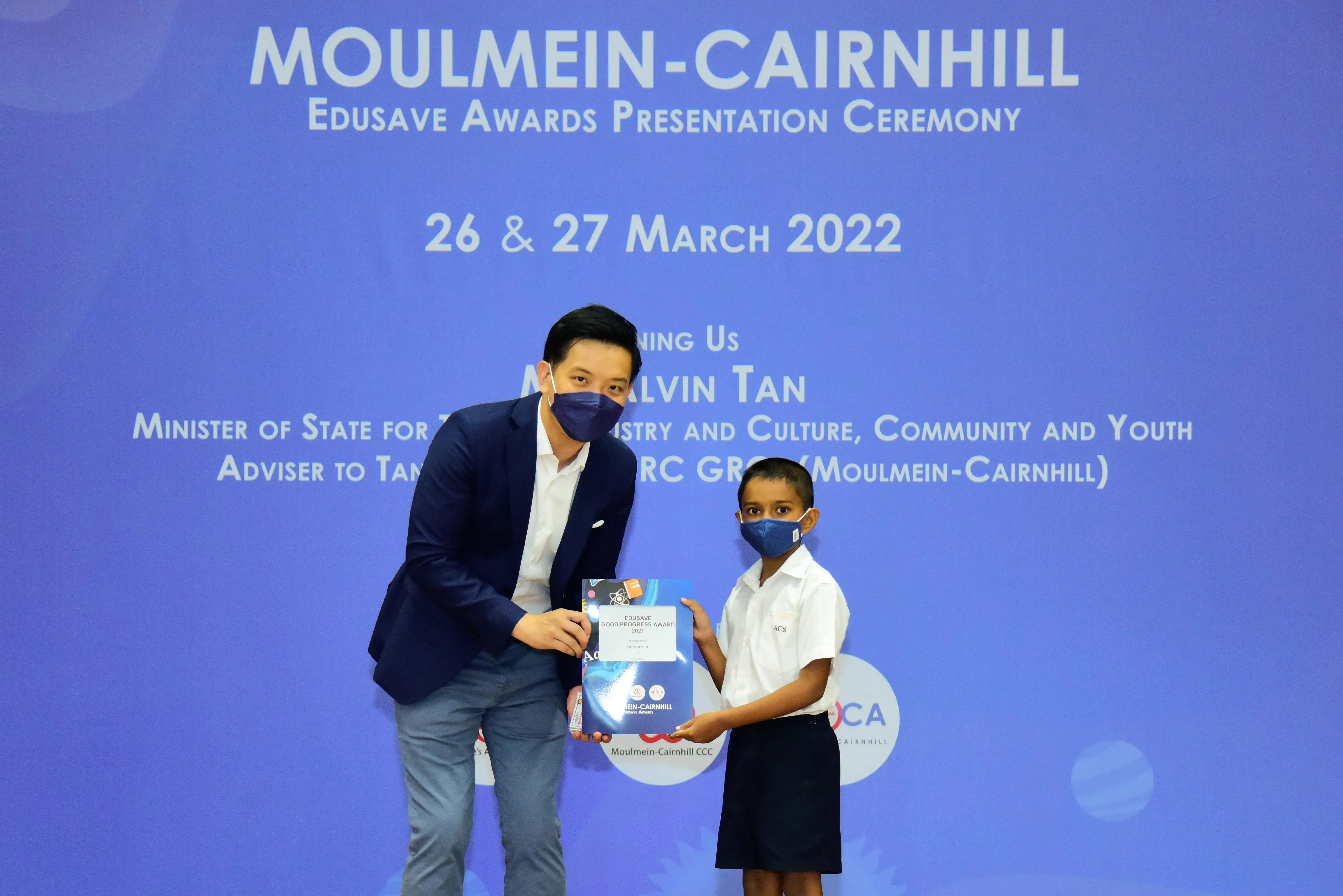 An adult and a young student in masks hold an award at the Moulmein-Cairnhill Edusave Awards Ceremony, March 2022.