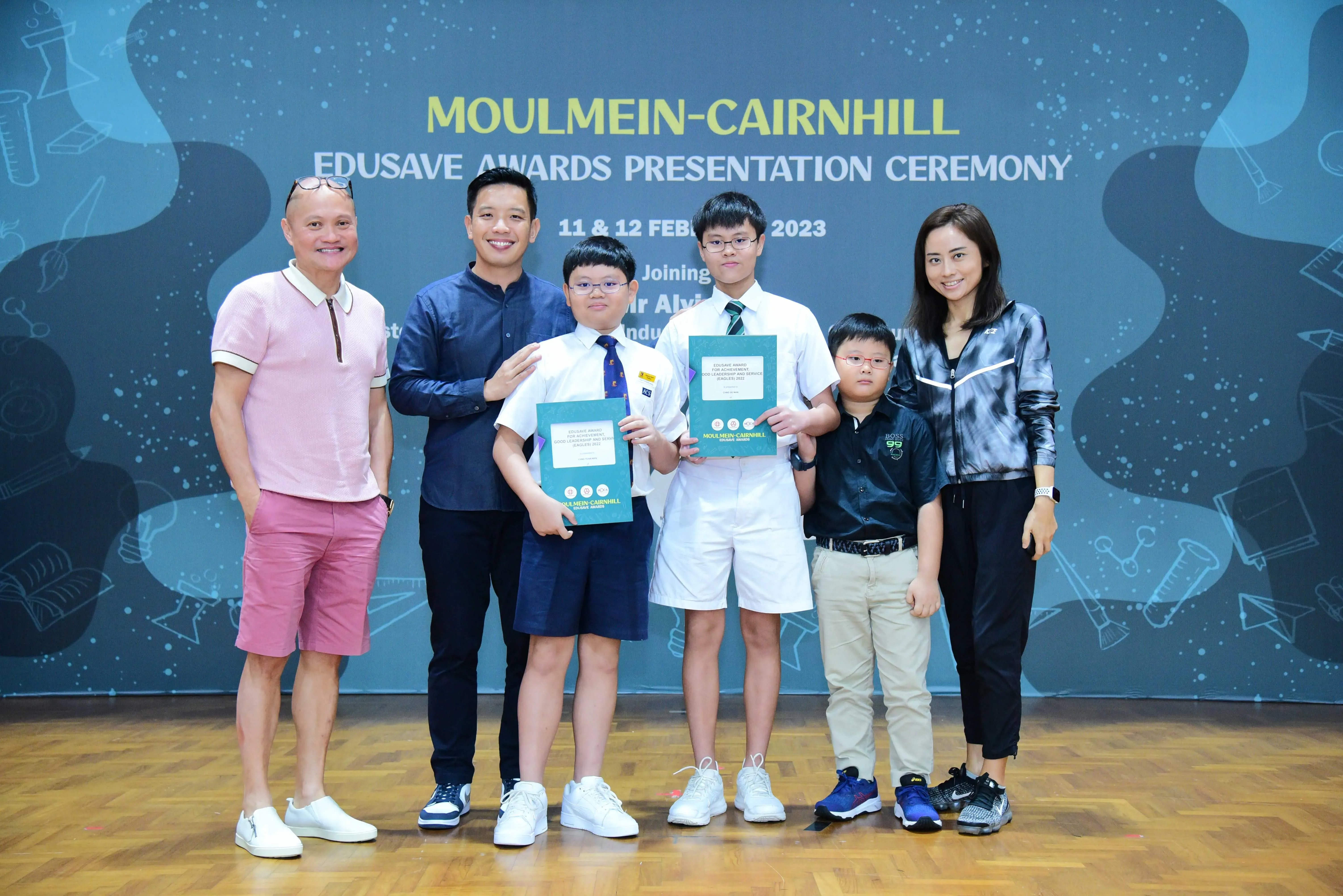 Six people pose at the Moulmein-Cairnhill Edusave Awards Presentation Ceremony 2023, two boys holding award folders.