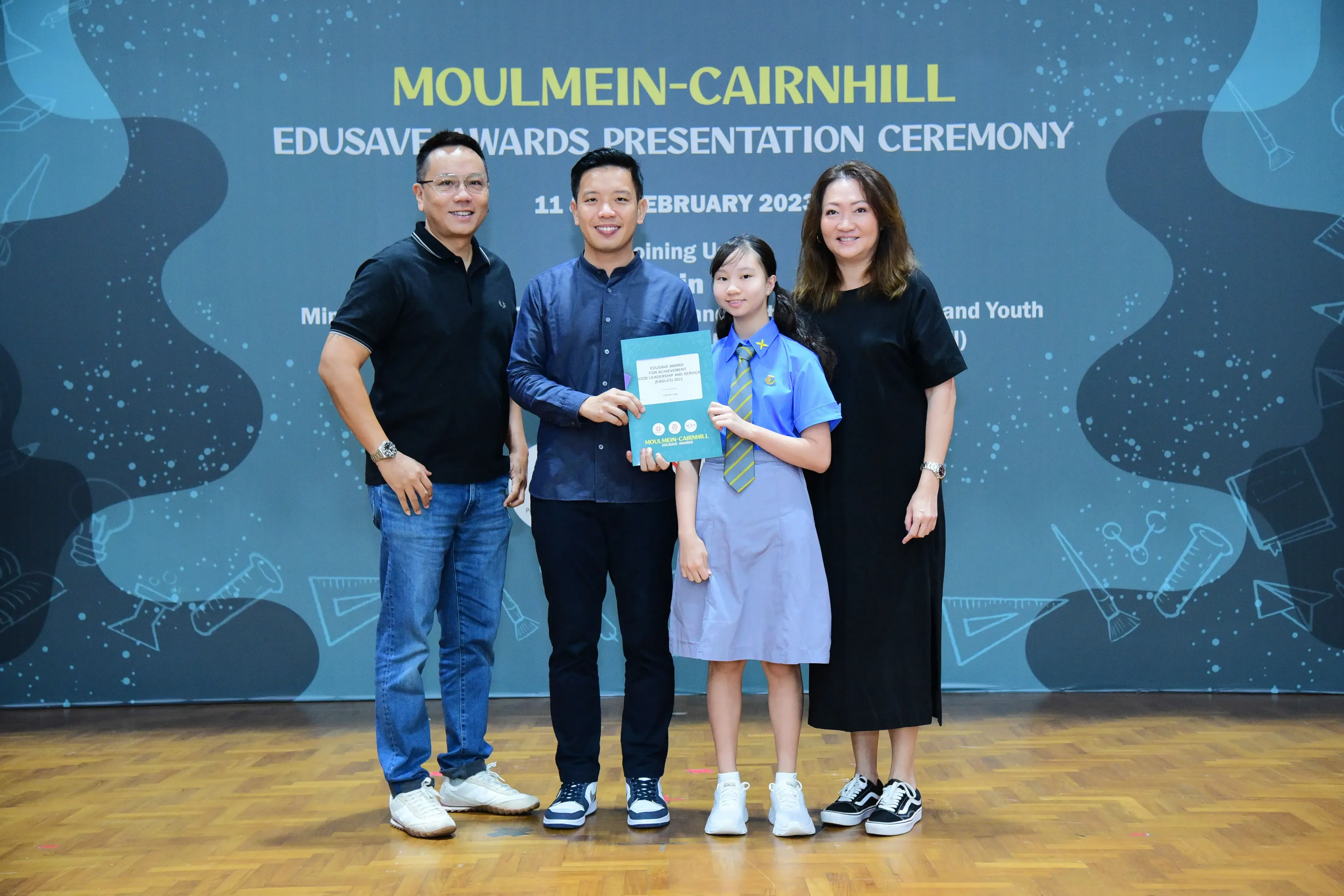 Three adults and a student in school uniform pose holding a certificate at Moulmein-Cairnhill Edusave Awards Ceremony.