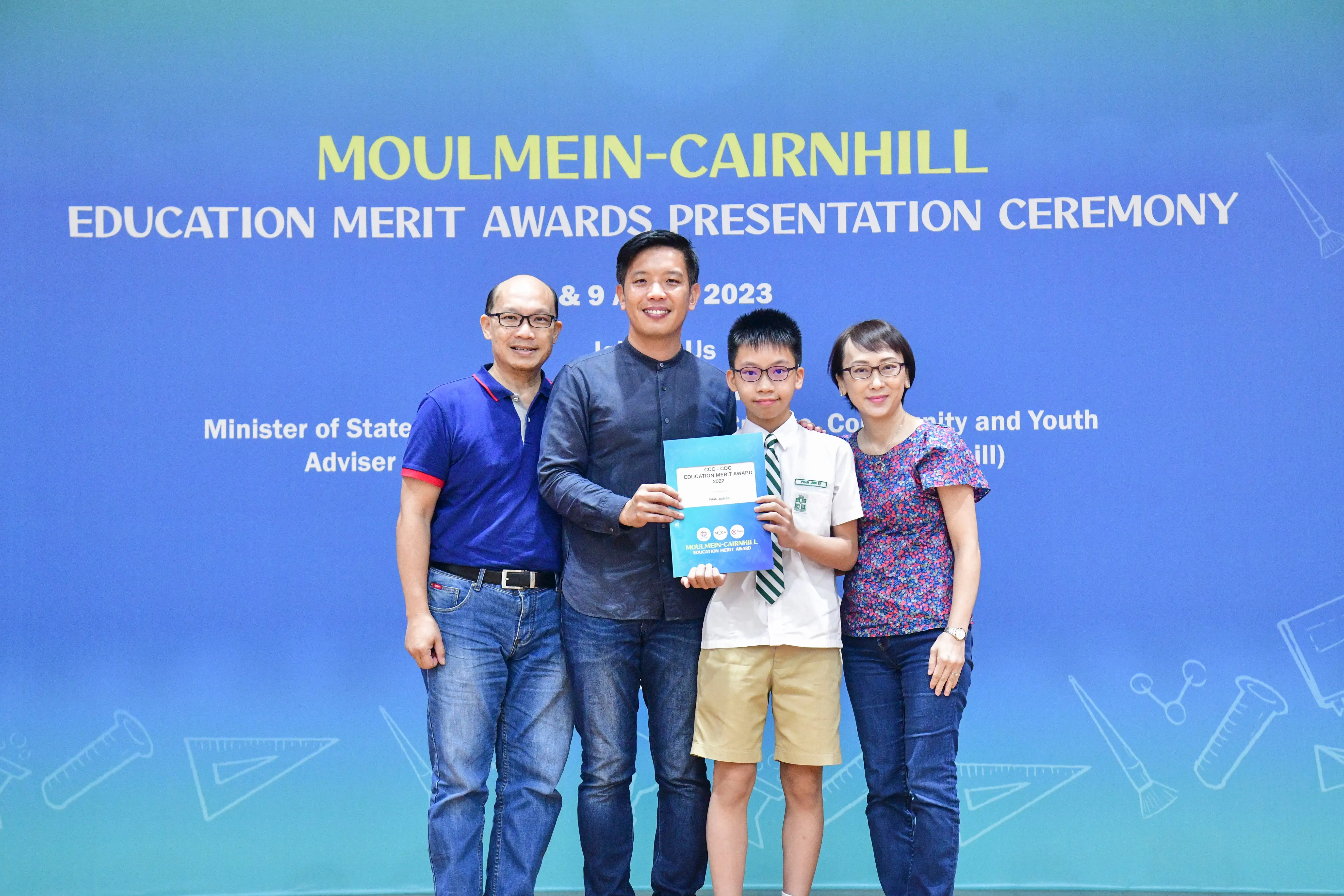 Four people pose at the Moulmein-Cairnhill Education Merit Awards Presentation Ceremony 2023, boy holding a certificate.