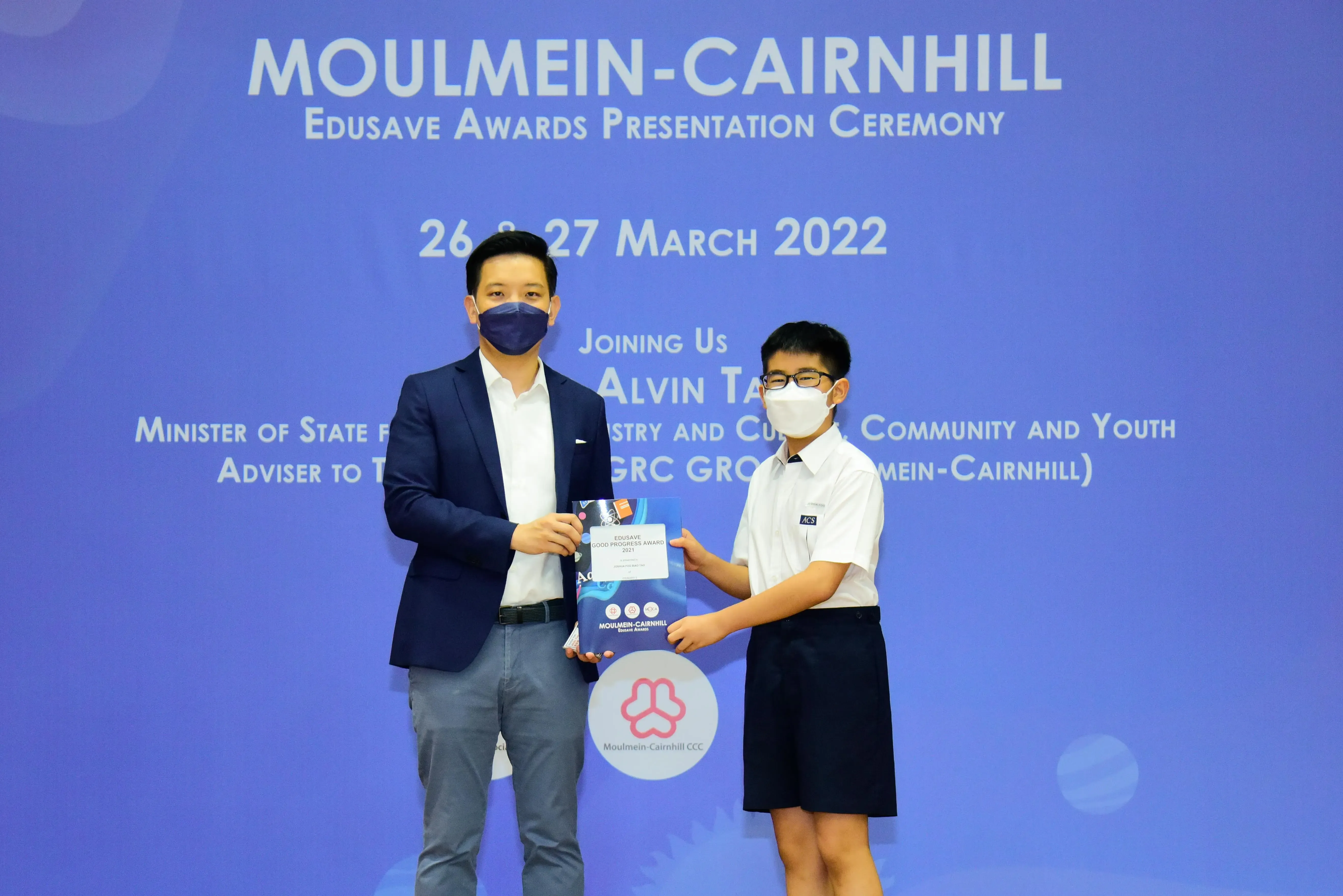 Two masked individuals hold an award certificate at the Moulmein-Cairnhill Edusave Awards Ceremony, March 2022.