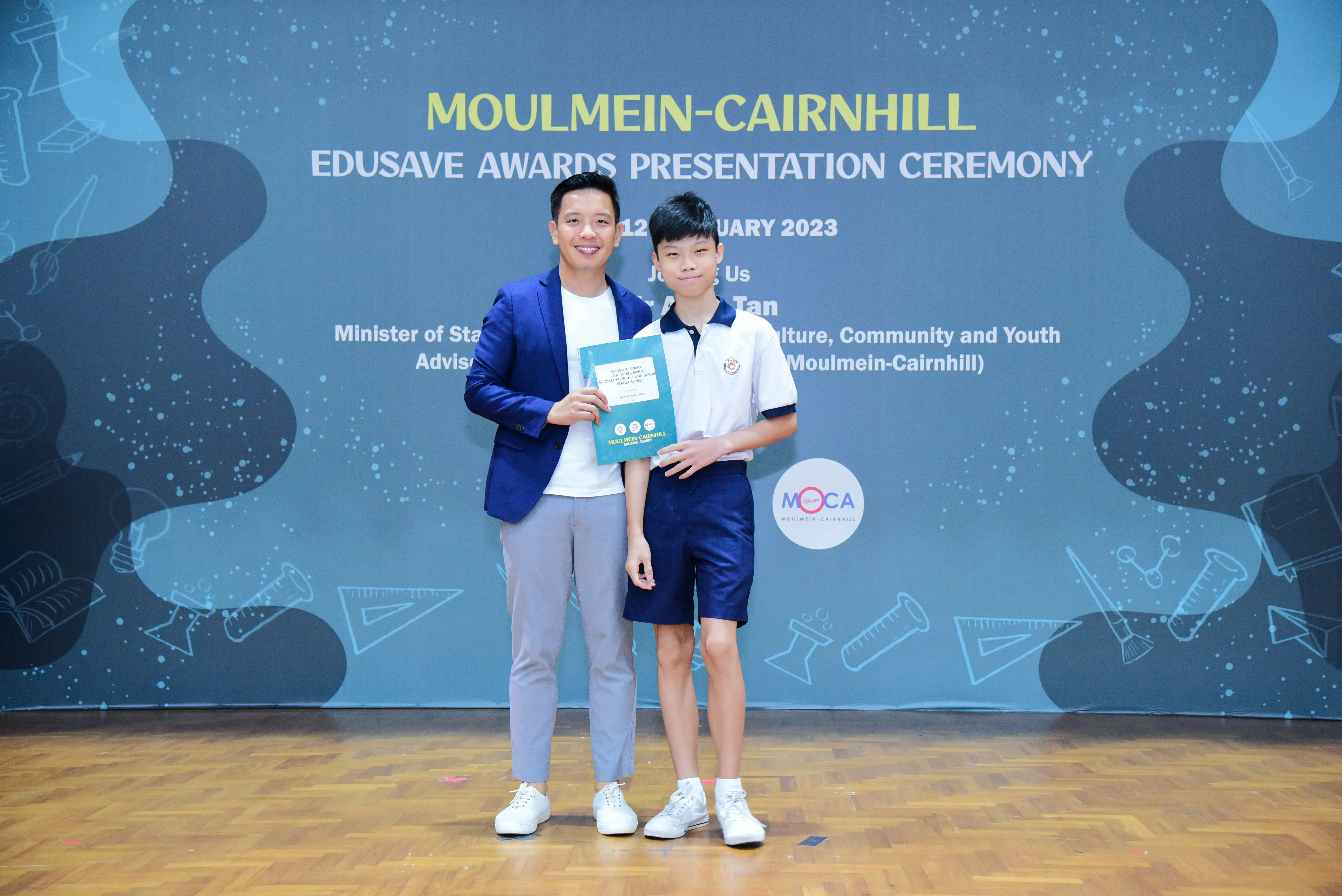 A man in a blue blazer and a young boy in school uniform pose together at the Moulmein-Cairnhill Edusave Awards Ceremony 2023.