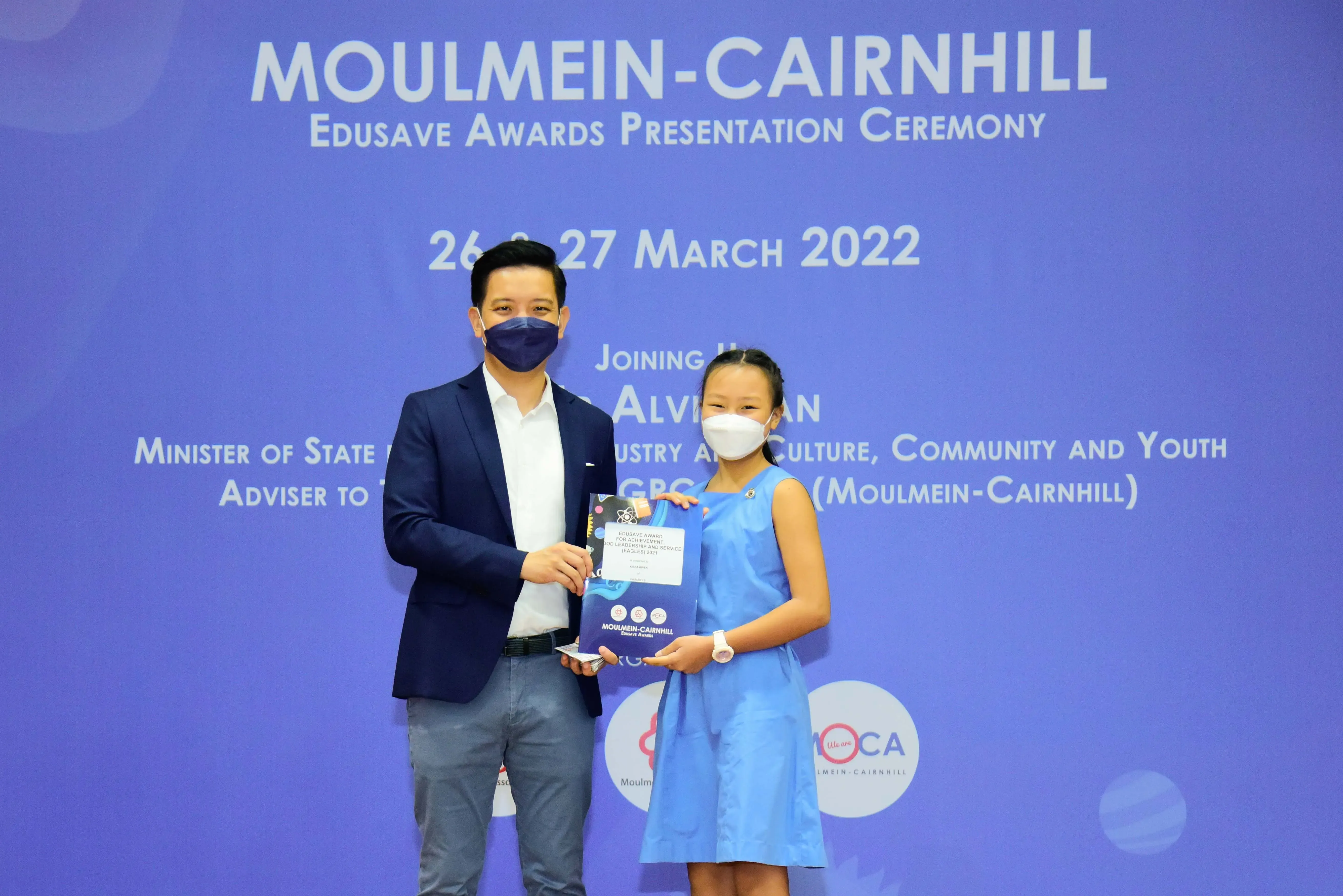 An adult and a child wearing masks hold an award at the Moulmein-Cairnhill Edusave Awards Ceremony, March 2022.