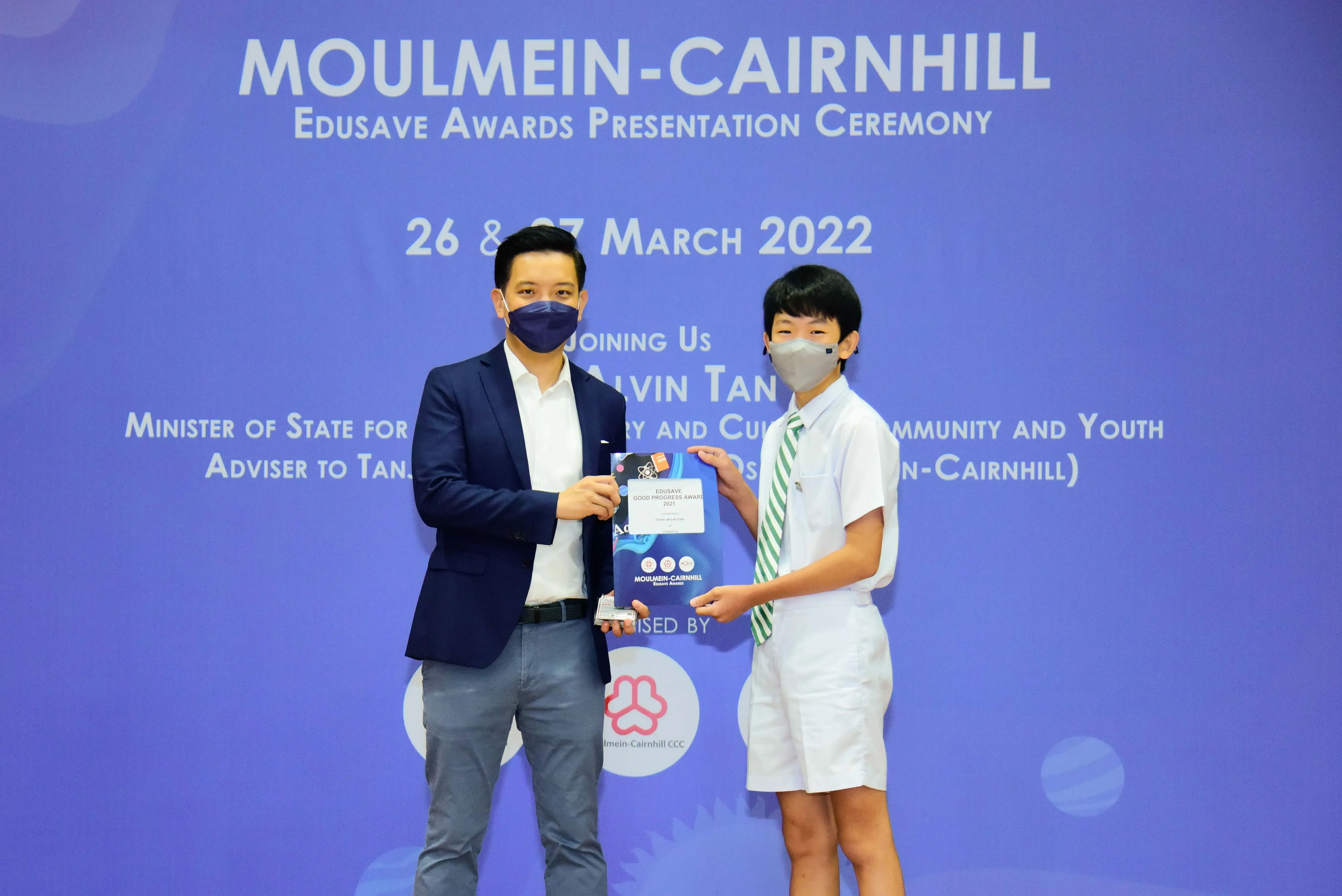An adult and a young student in school uniform hold an award together at the Moulmein-Cairnhill Edusave Awards Ceremony 2022.