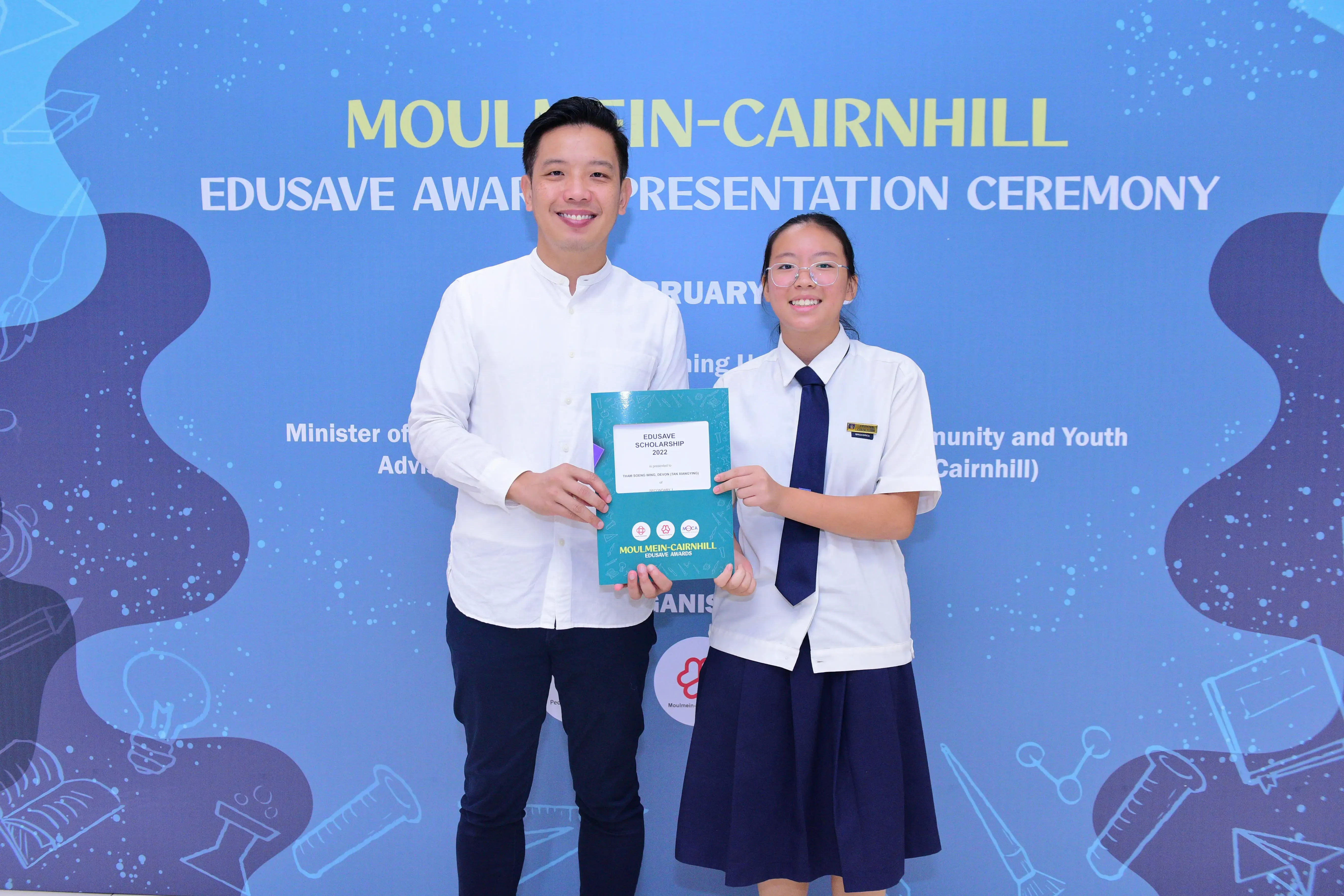 Two people smile holding an Edusave Scholarship certificate at the Moulmein-Cairnhill Award Presentation Ceremony.