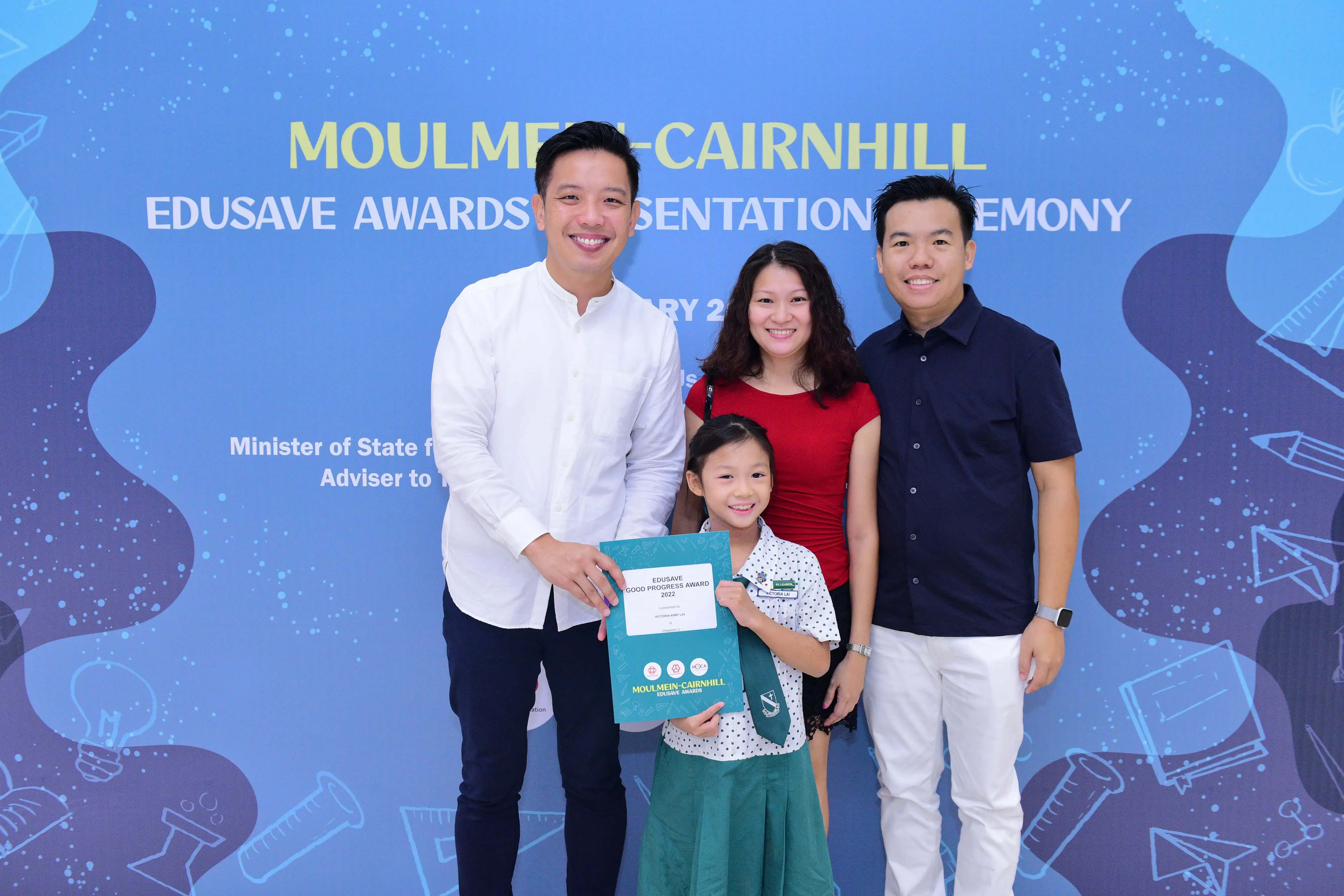 Three adults and a young girl pose holding an Edusave Good Progress Award certificate at Moulmein-Cairnhill ceremony.