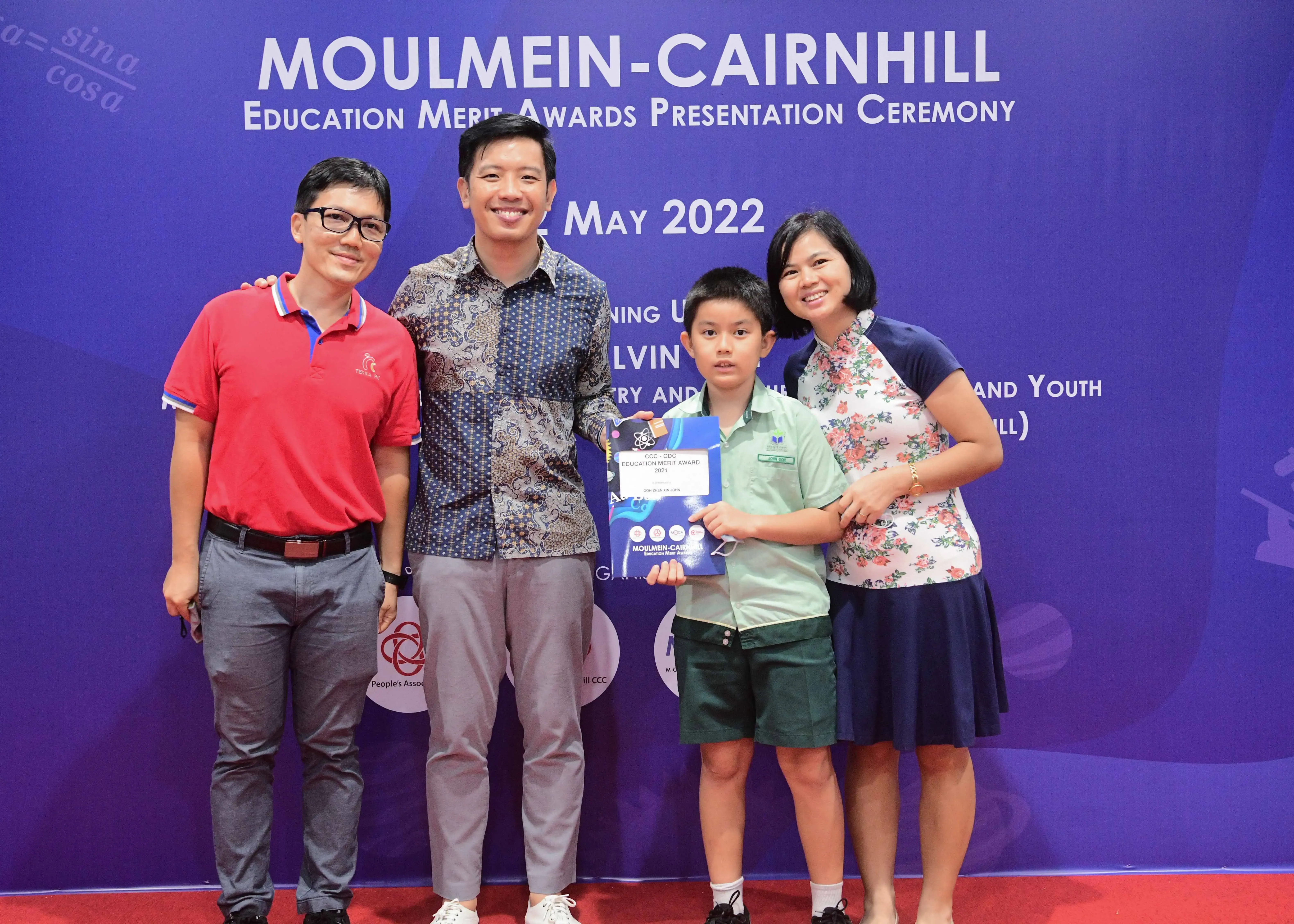 Four people pose at the Moulmein-Cairnhill Education Merit Awards Presentation Ceremony in May 2022, with a boy holding a certificate.