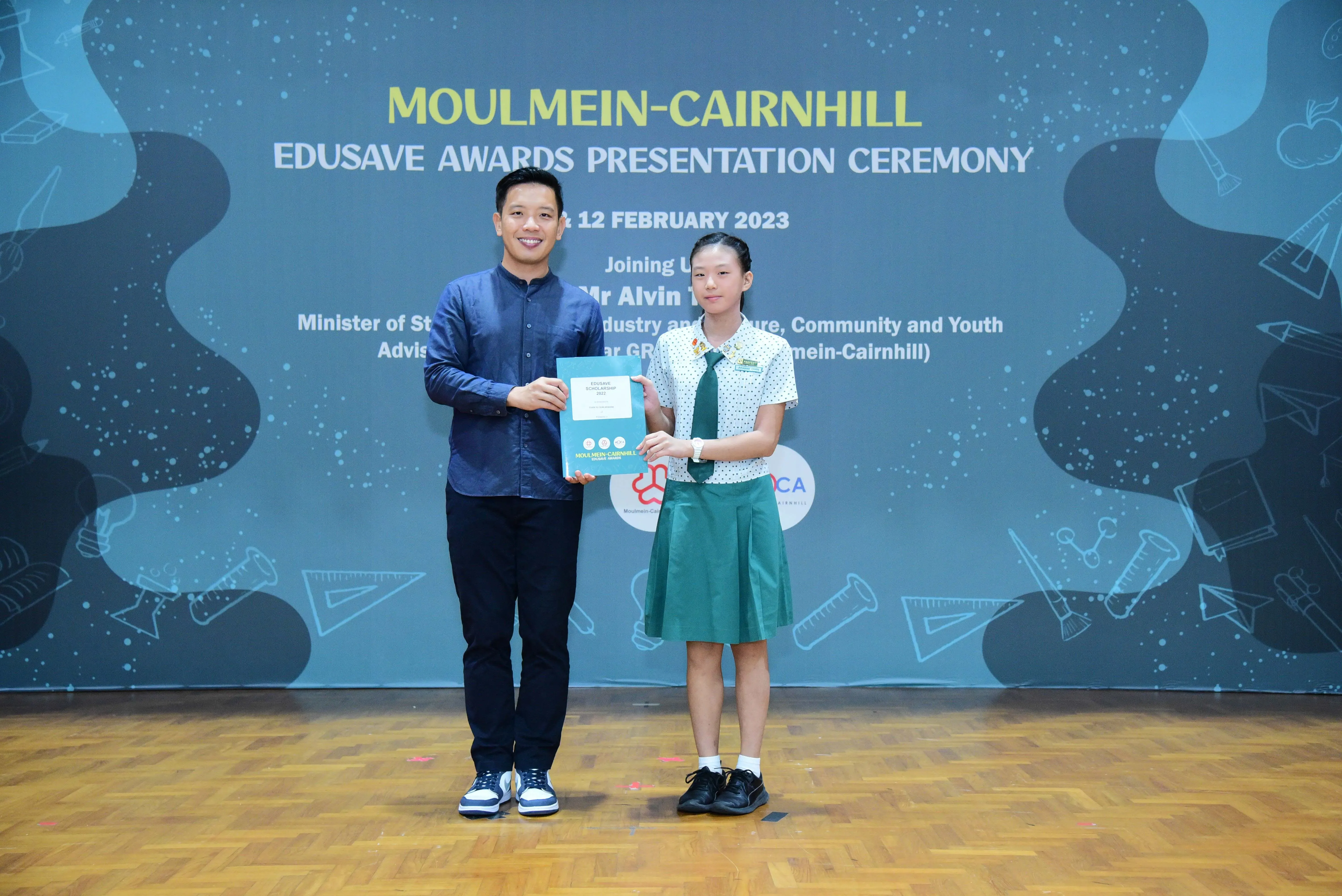 A man and a young girl in school uniform hold an award together at the Moulmein-Cairnhill Edusave Awards Ceremony 2023.