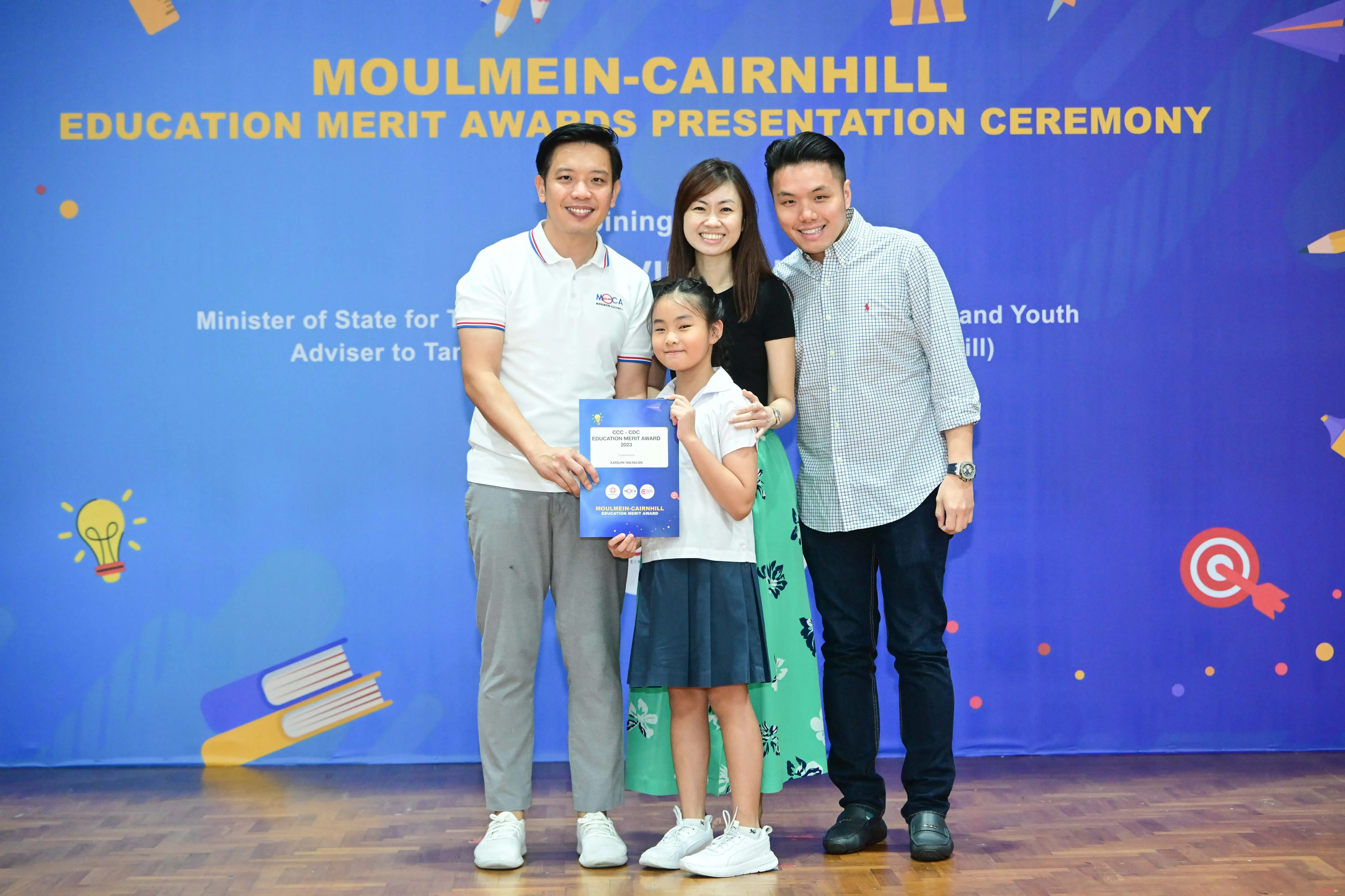Three adults and a young girl holding a certificate pose at the Moulmein-Cairnhill Education Merit Awards Ceremony.