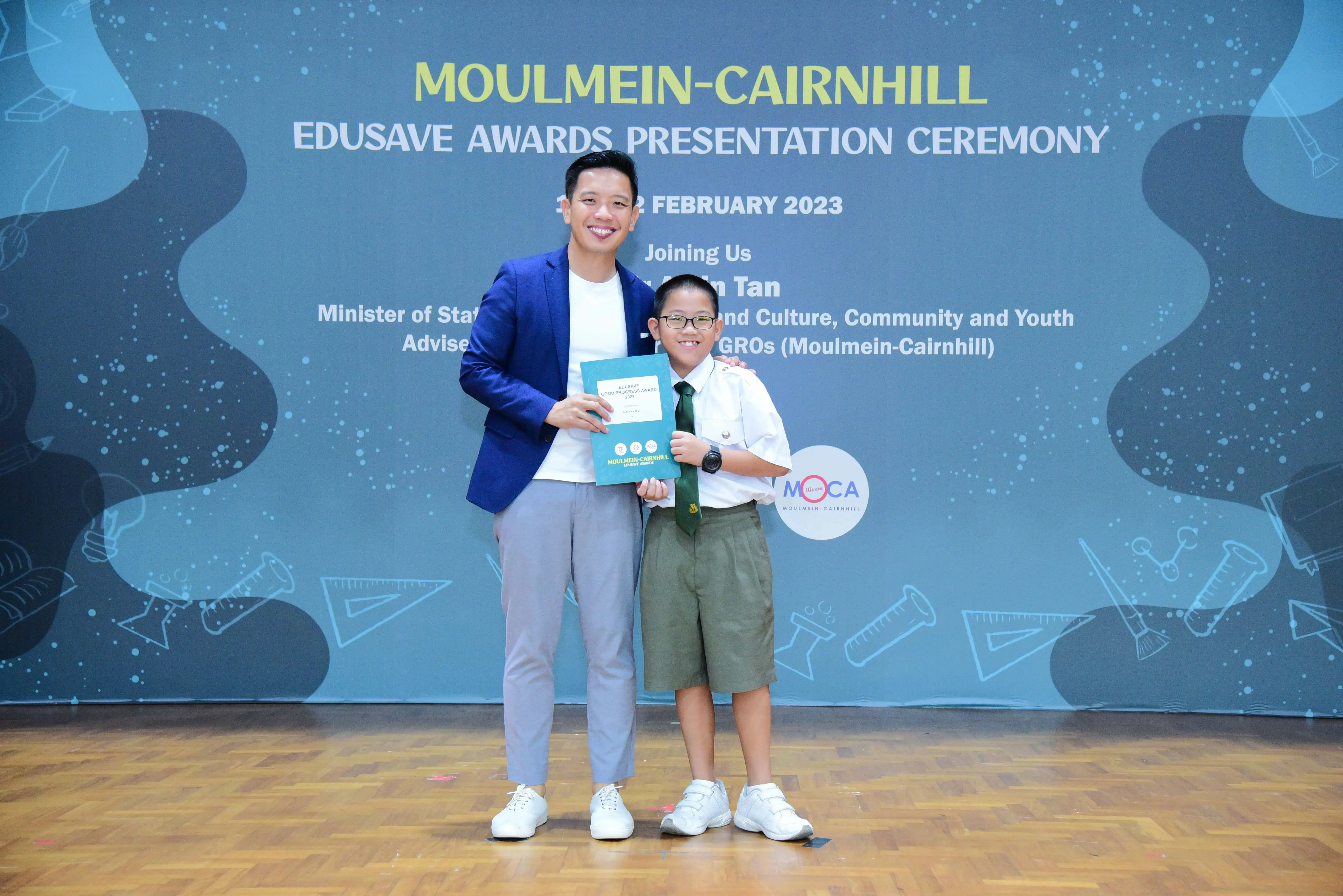 A man in a blue blazer and a young boy in school uniform pose at the Moulmein-Cairnhill Edusave Awards Ceremony 2023.