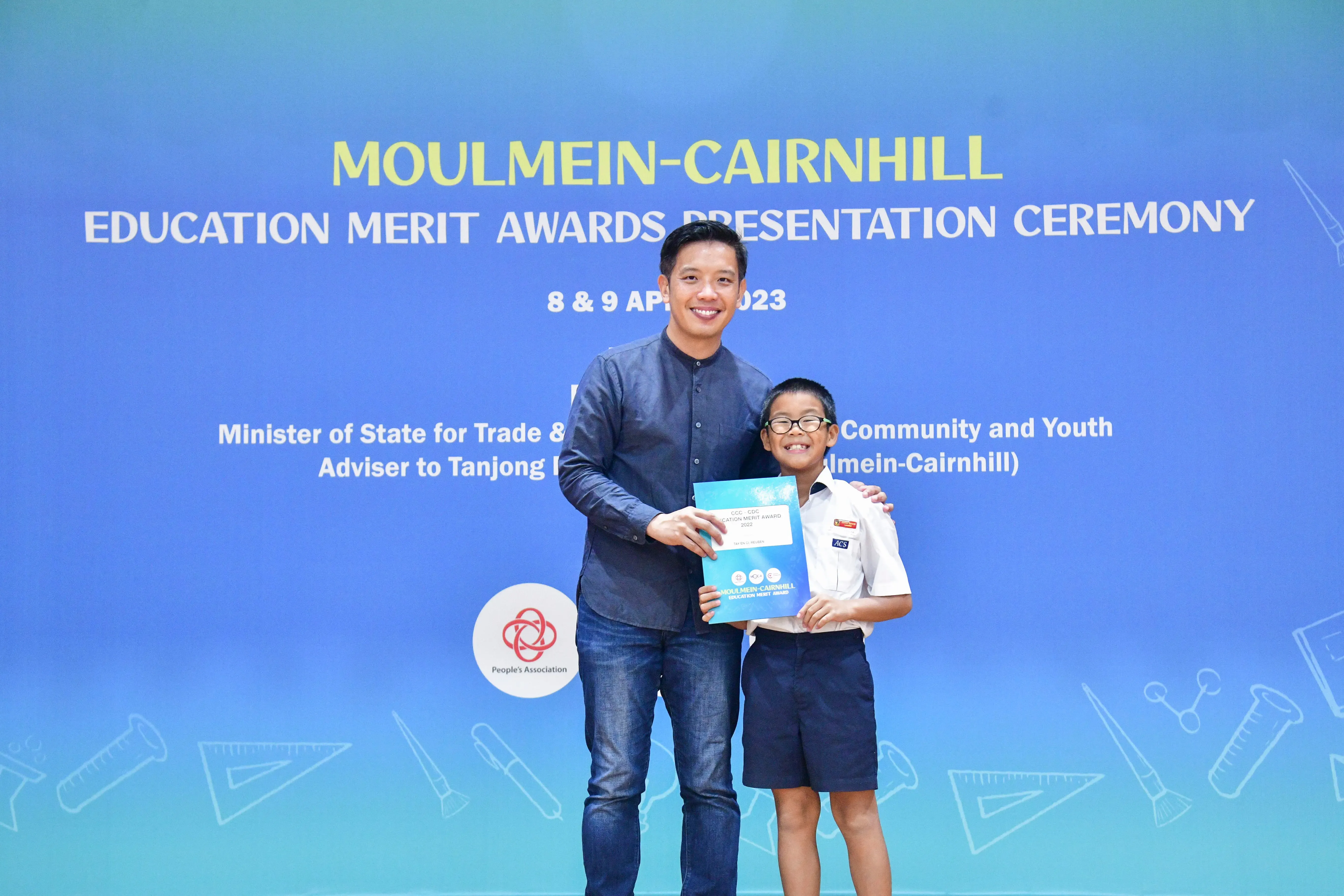 A man and a young boy in school uniform hold an award at the Moulmein-Cairnhill Education Merit Awards 2023.