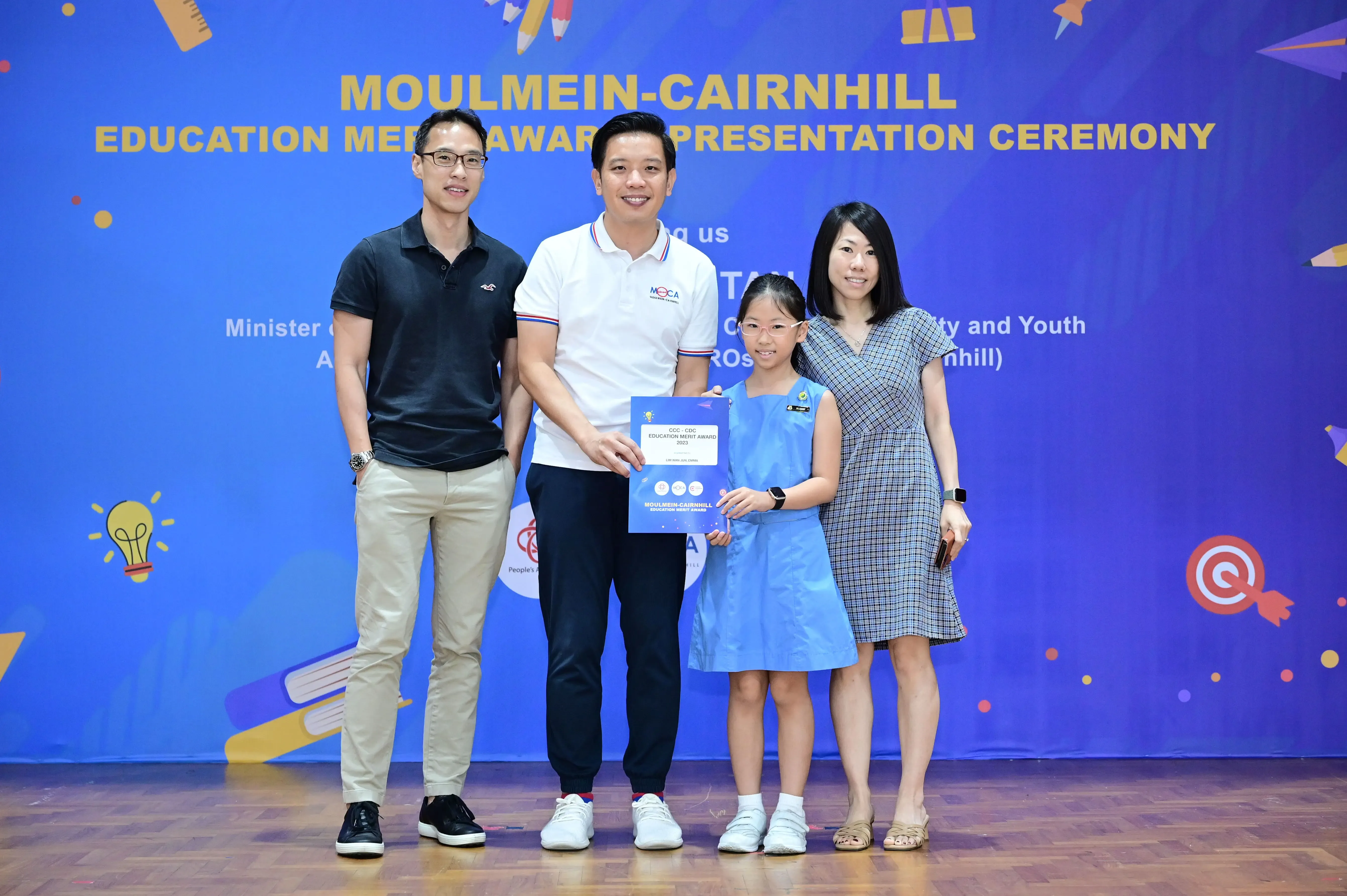 Three adults and a young girl pose holding an award certificate at the Moulmein-Cairnhill Education Merit Award Ceremony.