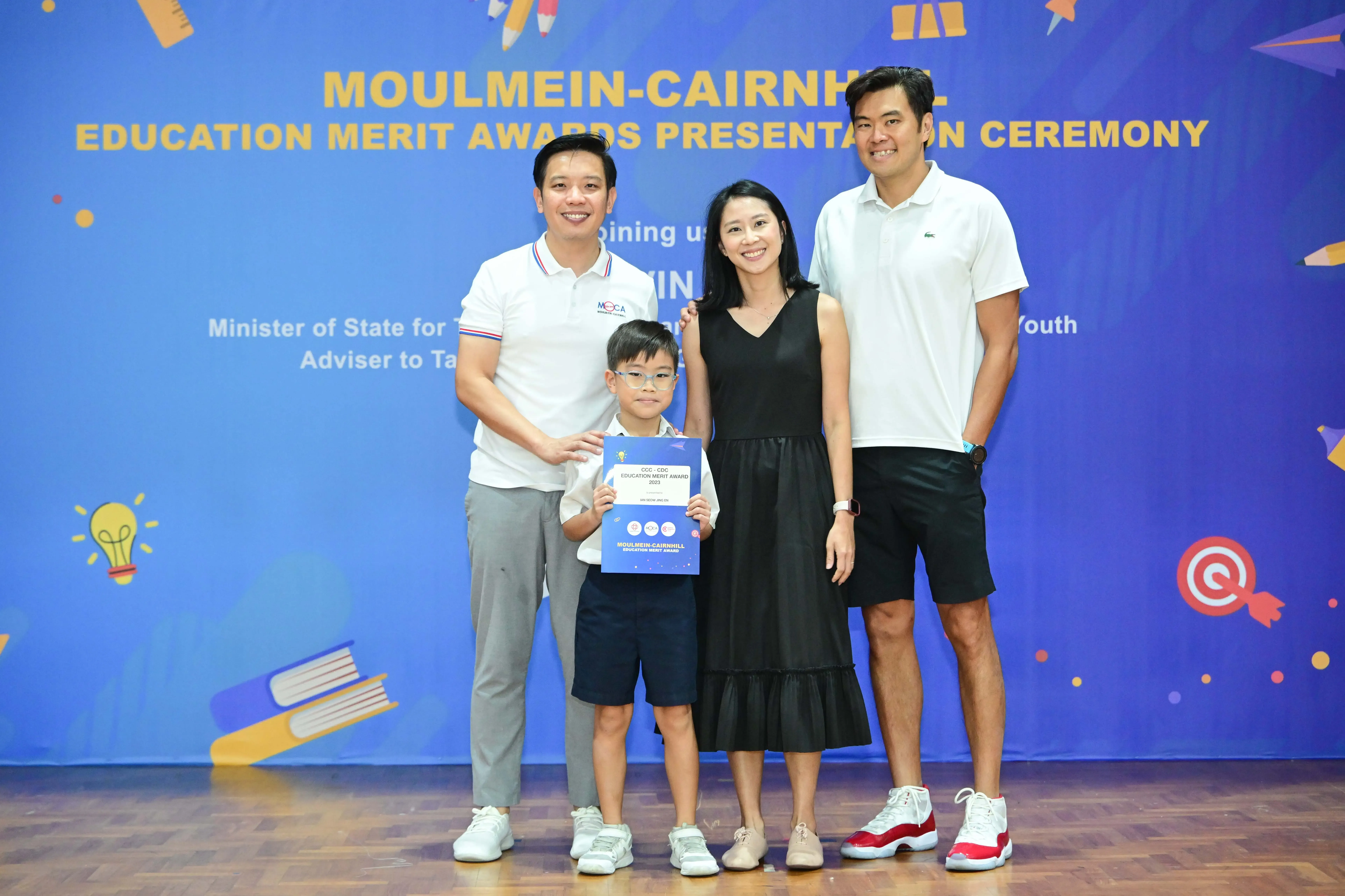 Three adults and a young boy holding a certificate pose at the Moulmein-Cairnhill Education Merit Awards ceremony.